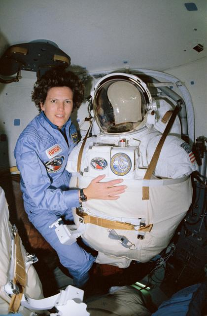 NASA image: STS-31 MS Sullivan poses next to stowed EMU in OV-103's airlock