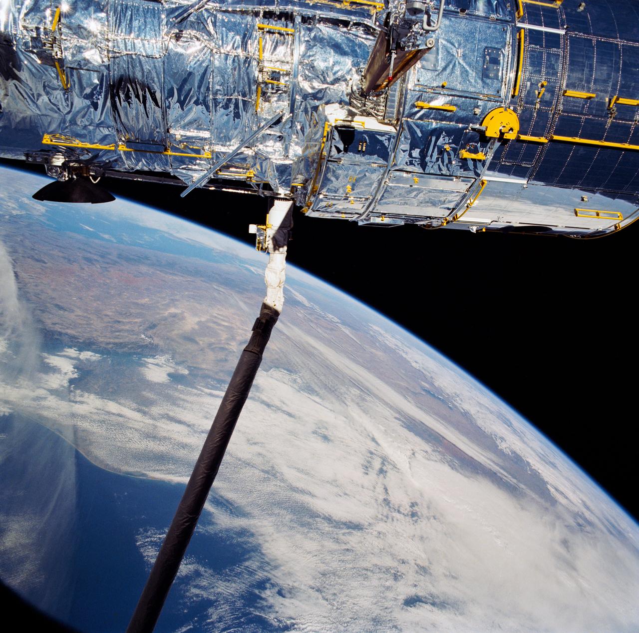 During STS-31, the Hubble Space Telescope (HST) is held in appendage deploy position by Discovery's, Orbiter Vehicle (OV) 103's, remote manipulator system (RMS) above the payload bay (PLB) and crew compartment cabin. While in this position the solar array (SA) wing bistem cassette (HST center) is deployed from its stowed location along side the Support System Module (SSM) forward shell. A high gain antenna (HGA) remains stowed along the SSM. The Earth's surface and the Earth limb creates a dramatic backdrop.