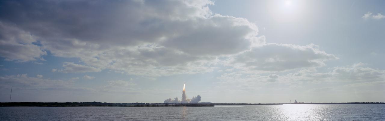 In this distant view, STS-31 Discovery, Orbiter Vehicle (OV) 103, is seen as it heads skyward after liftoff from Kennedy Space Center (KSC) Launch Complex (LC) Pad 39B at 8:33:51.0492 am (Eastern Daylight Time (EDT)). OV-103's silhouette atop the external tank (ET) appears above the glow of the solid rocket booster (SRB) and space shuttle main engine (SSME) firings. An exhaust plume trails behind and covers the launch pad area below the orbiter. A nearby waterway reflects the SRB/SSME glow in the foreground. At the far right and barely discernible is KSC LC Pad 39A and the Sound Supression Water System tower. Columbia, OV-102, is on LC Pad 39A which is separated by a distance of 1.6 miles. This was the first time since January 1986 that there was a shuttle on each pad.