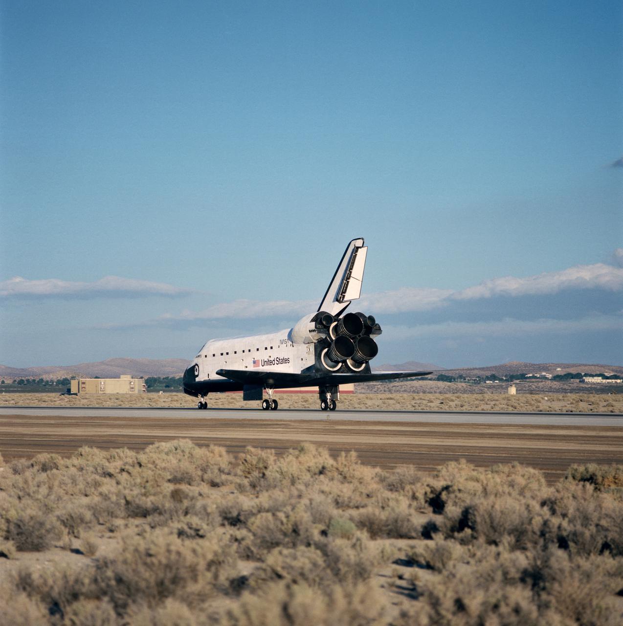 STS-31 Discovery, Orbiter Vehicle (OV) 103, rolls along concrete runway 22 at Edwards Air Force Base (EAFB), California, after nose landing gear (NLG) and main landing gear (MLG) touchdown. This view looks down OV-103's port side from the space shuttle main engines (SSMEs) to the nose section. The SSMEs are gimbaled to their descent position and the rudder/speedbrake is deployed on the vertical stabilizer. Wheel stop occurred at 6:51 am (Pacific Daylight Time (PDT)). In the distance EAFB facilities are visible.