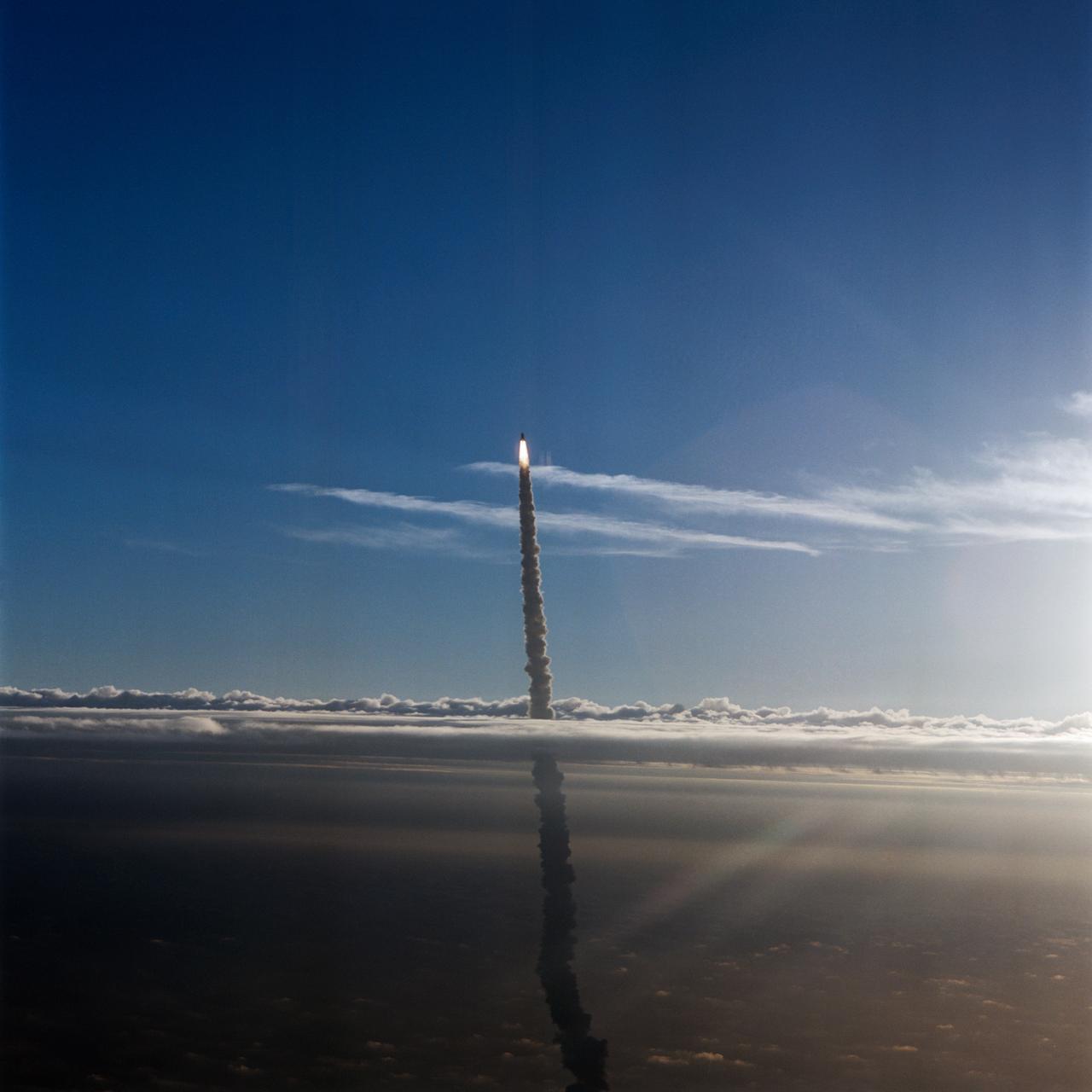 STS-32 Columbia, Orbiter Vehicle (OV) 102, pierces a layer of low lying clouds as it makes its ascent to Earth orbit for a 10-day mission. In this air-to-air view, OV-102 rides atop the external tank (ET) with flames created by solid rocket boosters (SRBs) appearing directly underneath it and a long plume of exhaust smoke trailing behind it and extending to Kennedy Space Center (KSC) Launch Complex (LC) Pad 39A below. OV-102 left KSC LC Pad 39A at 7:34:59:98 am Eastern Standard Time (EST) some 24 hours after dubious weather at the return-to-landing site (RTLS) had cancelled a scheduled launch. The photo was taken by astronaut Michael L. Coats, acting chief of the Astronaut Office, from the Shuttle Training Aircraft (STA).