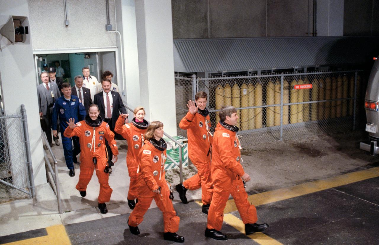 STS032-S-056 (20 Jan 1990) --- STS-32 Columbia, Orbiter Vehicle (OV) 102, crewmembers depart the Kennedy Space Center (KSC) Operations and Checkout (O and C) Building enroute to KSC Launch Complex (LC) Pad 39A. Dubious weather at the return-to-launch site (RTLS) caused postponement of yesterday's planned launch. From left to right are Mission Specialist (MS) G. David Low, MS Marsha S. Ivins, MS Bonnie J. Dunbar, Pilot James D. Wetherbee, and Commander Daniel C. Brandenstein. All crewmembers are wearing launch and entry suits (LESs) and Low, Ivins, and Wetherbee wave to spectators as they head to the transportation van. Following the crew are astronaut Michael L. Coats (left) and NASA/JSC manager Donald R. Puddy.