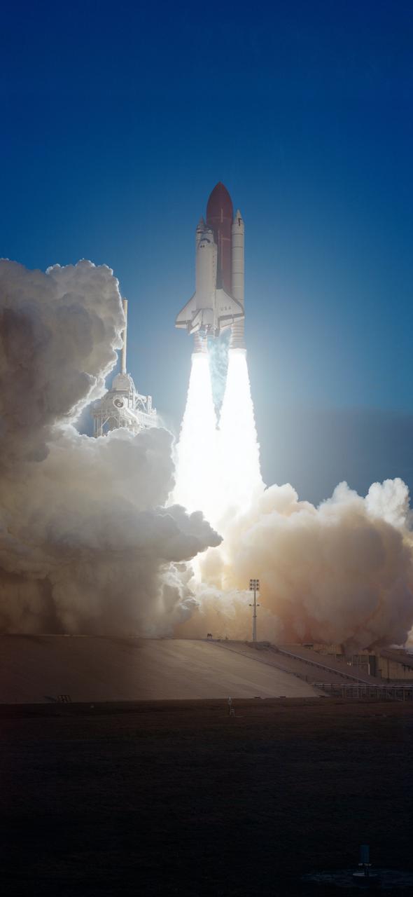 STS-32 Columbia, Orbiter Vehicle (OV) 102, atop the external tank (ET) and flanked by two solid rocket boosters (SRBs) rises above the mobile launcher platform and is nearly clear of the fixed service structure (FSS) tower at Kennedy Space Center (KSC) Launch Complex (LC) Pad 39A. Plumes of smoke billow from the SRBs and cover the launch pad in a cloud. Liftoff occurred at 7:34:59:98 am Eastern Standard Time (EST) some 24 hours after dubious weather at the return-to-landing site (RTLS) had cancelled a scheduled launch. OV-102's launch is highlighted against the early morning darkness.