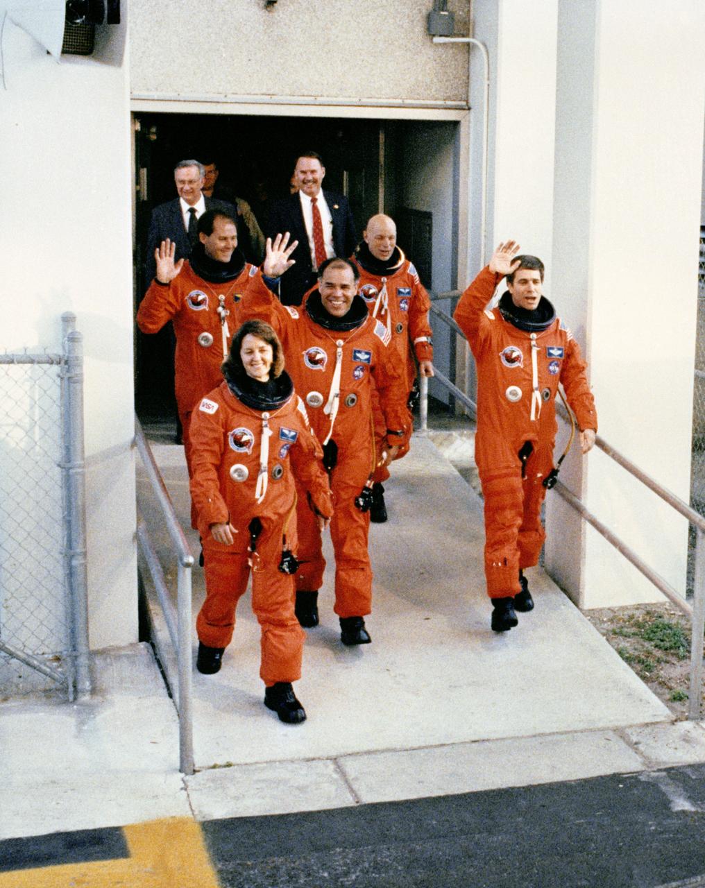 STS033-S-009 (22 Nov 1989) --- Leaving the operations and checkout building for catching a van ride to the launch pad are the five astronaut crewmembers assigned to STS-33, a DOD-devoted mission.  Displaying smiles and waves for the crowd on hand are (left to right) Astronauts Manley L. Carter, Kathryn C. Thornton; Frederick D. Gregory,  commander; F. Story Musgrave and John E. Blaha.  Behind them are (left to right), Olan J. Bertrand, Michael L. Coats (partially obscured) and Donald R. Puddy of the Johnson Space Center (JSC).