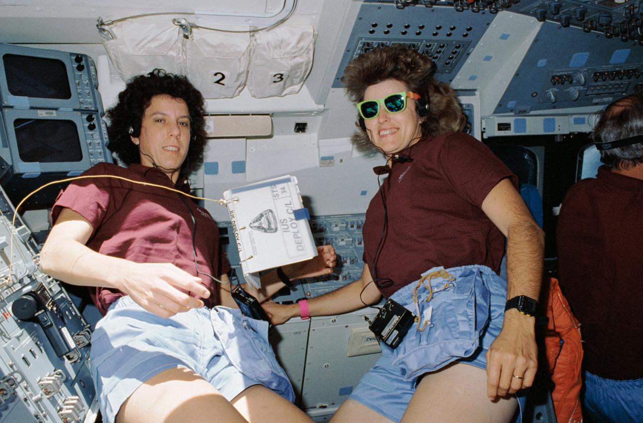 STS034-09-007 (23 Oct. 1989) --- Having been in space only a few hours, three of the STS-34 astronaut crew prepare for pre-deployment exercises involving one of the most prominent "passengers" of the flight -- the Galileo payload which was lying in Atlantis', Orbiter Vehicle (OV) 104's, payload bay (PLB). Pictured, left to right, are astronauts Ellen S. Baker and Shannon W. Lucid, both mission specialists; along with Donald E. Williams, commander, who guided OV-104's course during the exercise. Baker and Lucid communicated with ground controllers while juggling other Galileo-related chores. Both Baker and Lucid are equipped with SONY Walkmans and are wearing headsets. Lucid wears a pair of sunglasses with brightly colored frames. A tethered inertial upper stage (IUS) deploy checklist (C/L) floats between the two and a spotmeter is Velcroed to an on orbit station control panel.