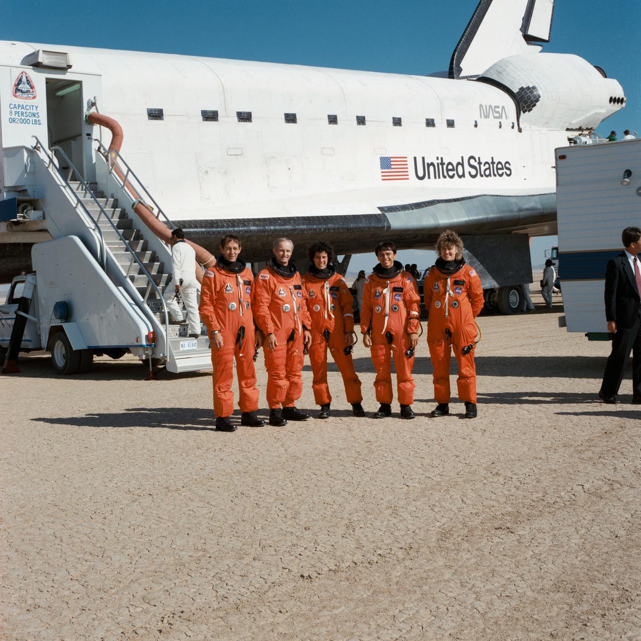 STS-34 crewmembers, wearing launch and entry suits (LESs), stand in front of Atlantis, Orbiter Vehicle (OV) 104, on Runway 23 dry lake bed at Edwards Air Force Base (EAFB), California. Left to right are Pilot Michael J. McCulley, Commander Donald E. Williams, Mission Specialist (MS) Ellen S. Baker, MS Franklin R. Chang-Diaz, and MS Shannon W. Lucid. Ground crews service OV-104 in the background.