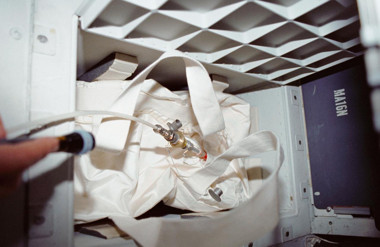 STS035-12-005 (2-10 Dec 1990) --- During STS-35, middeck stowage volume G and a contingency water container (CWC) were utilized to remedy a problem onboard Columbia, Orbiter Vehicle (OV) 102. A hose connecting OV-102's waste water system to the CWC was used in order to bypass a suspected clog in the line from the waste water tank to the exit nozzle. On flight day seven, Pilot Guy S. Gardner carried out an inflight maintenance (IFM) procedure by connecting a spare hose from the line to the container. The CWC is a rubber-lined duffle bag that holds about 95 pounds of water and is used in situations where water cannot be dumped overboard normally.