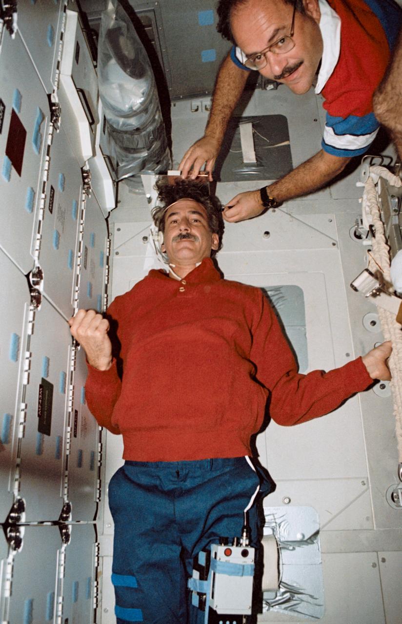 STS035-19-021 (December 1990) ---  STS-35 Mission Specialist  Jeffrey A. Hoffman stretches out on the middeck floor while MS John M. (Mike) Lounge records his height. The two crew members are in front of the forward lockers aboard Columbia, Orbiter Vehicle (OV) 102. Hoffman steadies himself using the stowed treadmill and the lockers. Above Hoffman's head is a plastic bag filled with Development Test Objective (DTO) 634, Trash Compaction and Retention System Demonstration, trash compactor charcoal filtered bag lids. This image was selected by the Public Affairs Office (PAO) for public release.