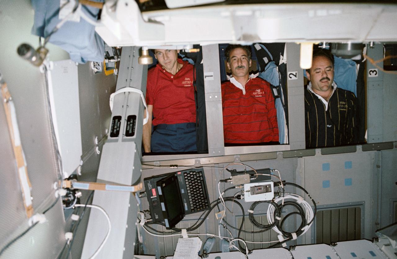Though they are not actually asleep, three STS-35 crewmembers demonstrate the bunk-style sleep compartments onboard Columbia's, Orbiter Vehicle (OV) 102's, middeck. From top to bottom are Payload Specialist Samuel T. Durrance, Mission Specialist (MS) Jeffrey A. Hoffman, and MS John M. Lounge. At the left is the shuttle amateur radio experiment (SAREX). The crew escape pole (CES) is visible overhead and the open airlock hatch in the foreground. The sleep station is located against the middeck starboard wall.
