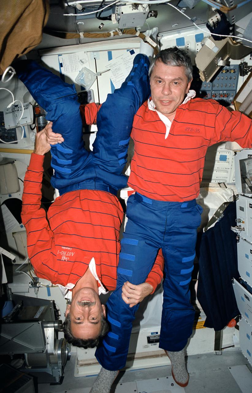 STS035-49-029 (2-10 Dec 1990) --- Posing on the middeck of Columbia, Orbiter Vehicle (OV) 102, are Mission Specialist (MS) Jeffrey A. Hoffman (mustache) and MS Robert A. R. Parker. Determining who is right side up is complicated by the microgravity of space. Hoffman's head is at the middeck floor and his feet are at the ceiling. The two crewmembers are in front of OV-102's port side with the waste collection system (WCS) contingency unit, side hatch, and galley visible behind them.