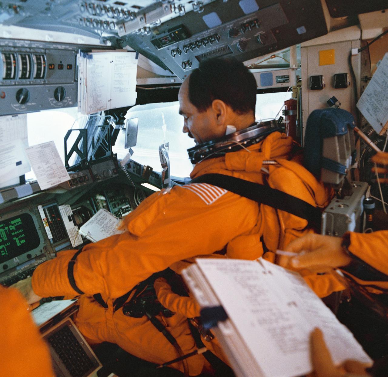 STS035-515-003 (2-10 Dec 1990) --- STS-35 Pilot Guy S. Gardner, wearing his launch and entry suit (LES), reviews descent checklist while at the pilots station on the forward flight deck of Columbia, Orbiter Vehicle (OV) 102. Crewmembers are conducting procedures related to the final stages of the mission and the landing sequence. Silhouetted in forward windows W4 and W5 are the head up display (HUD), flight mirror assembly, and a drinking water bag with straw.