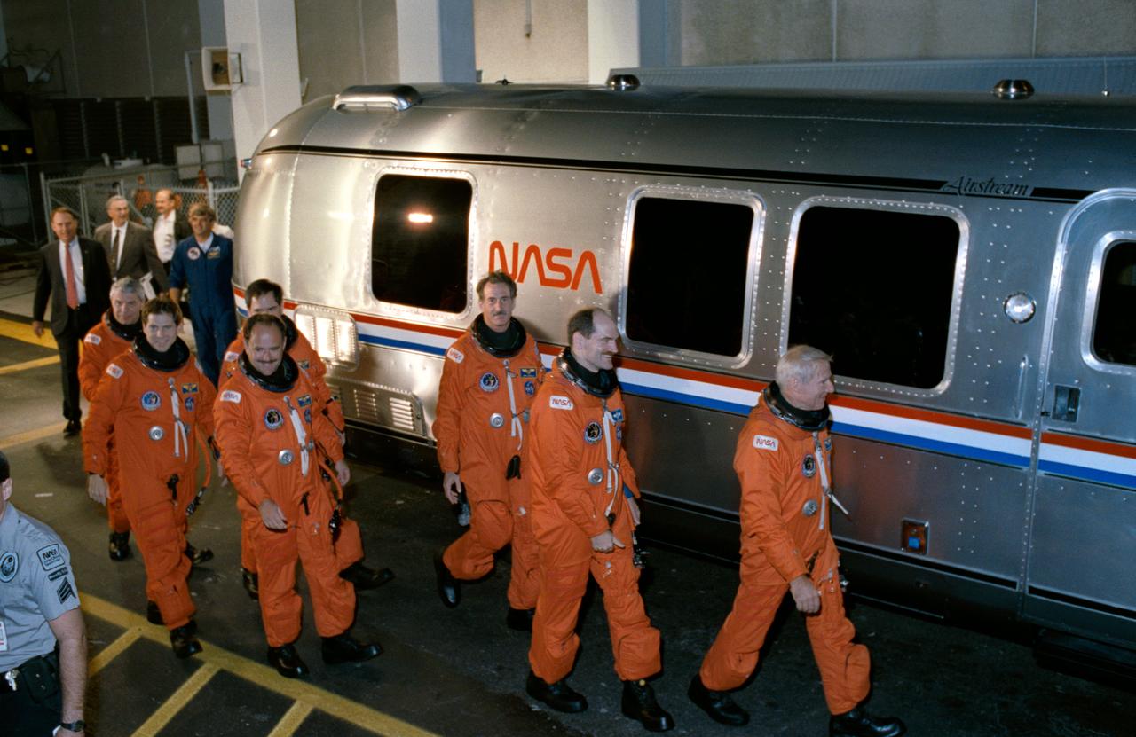 STS035-S-016 (2 Dec 1990) --- Astronaut Vance D. Brand, right, leads the STS 35 crew toward a transfer van that will take them from the nearby operations and checkout (O&C) building to Launch Complex 39.  Trailing the mission commander, left to right, are Robert A. R. Parker, Samuel T. Durrance, Ronald A. Parise, John M. (Mike) Lounge, Jeffrey A. Hoffman and Guy S. Gardner.