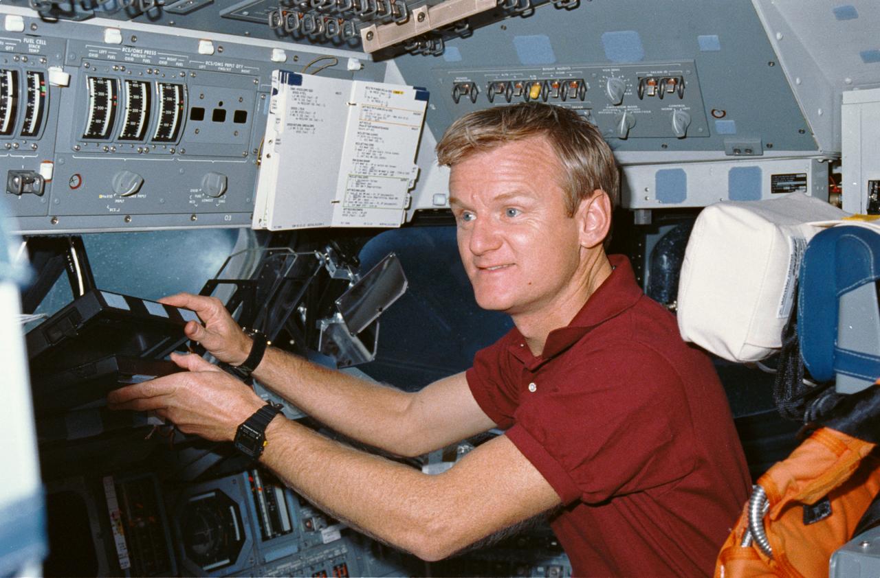 STS036-03-027 (3 March 1990) --- STS-36 Pilot John H. Casper reaches for the shuttle portable onboard computer (SPOC), a laptop computer, while at the pilots station on the forward flight deck of Atlantis, Orbiter Vehicle (OV) 104. Casper, seated in the pilot’s seat, lifts the SPOC from the forward window ledge. Appearing around him are forward crew compartment windows, the head up display (HUD), the flight mirror assembly, and a checklist attached to control panel O3. Casper and four other astronauts spent four days, 10 hours and 19 minutes aboard the spacecraft for a Department of Defense (DOD) devoted mission.