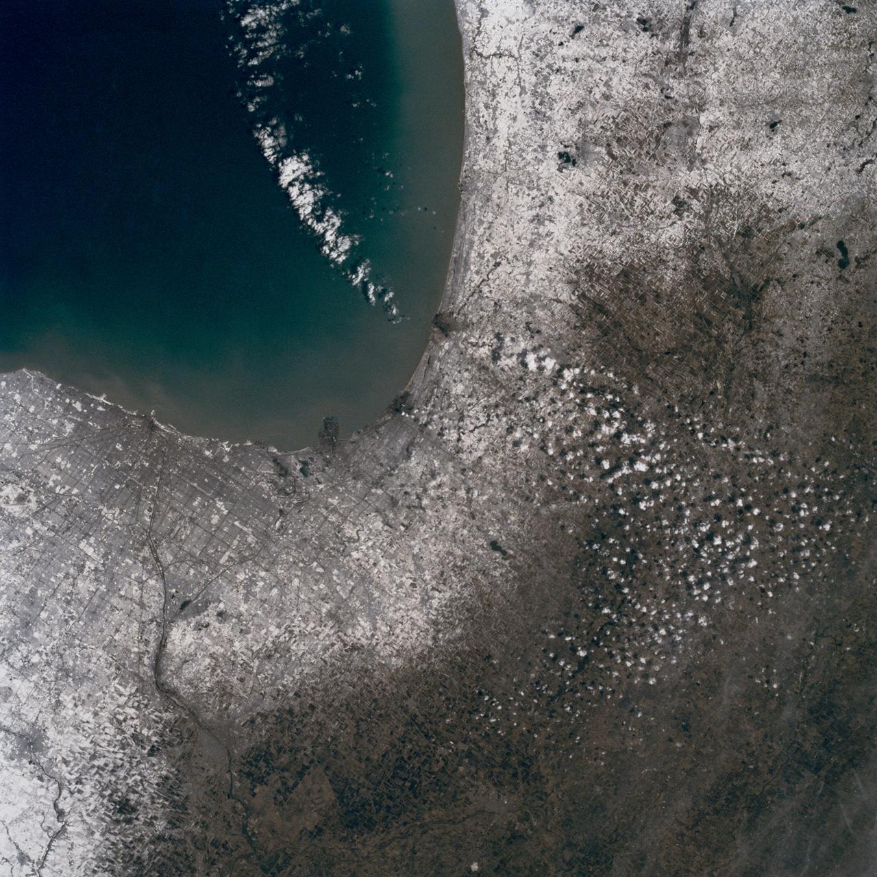 In this late winter scene of Chicago, Illinois, USA (41.5N, 87.0W) the light dusting of snow has actually enhanced the determination of the cities street pattern, parks and other cultural features. Sited at the south end of Lake Michigan, Chicago has long served as an industrial, transportation and communications center for the midwest. The obvious snowline on the ground enables meteorologists to trace the regional groundtracks of winter storms.