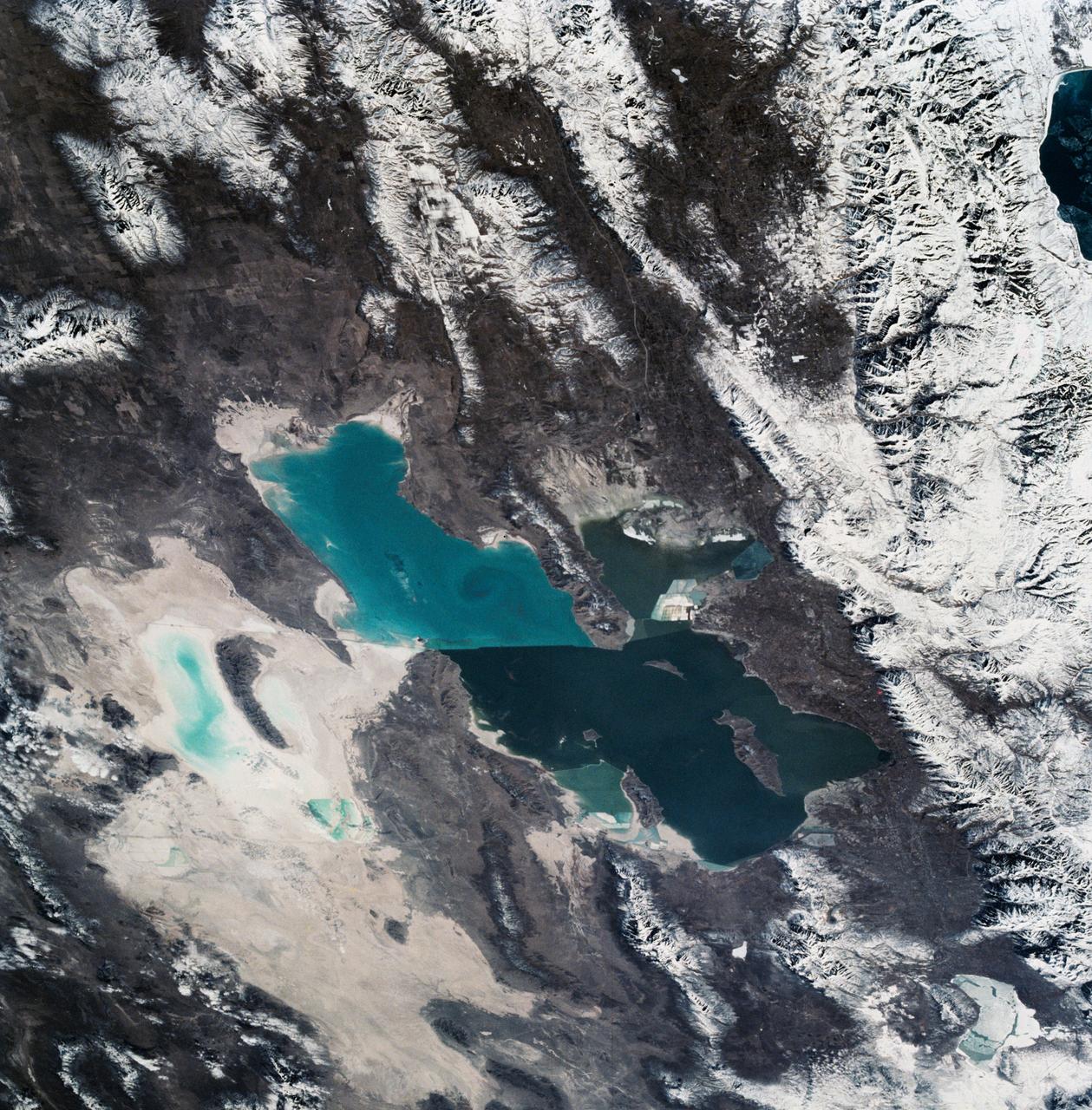 As seen from space, the Great Salt Lake, Utah, USA (41.5N, 112.5W) appears as two separate bodies of water with a narrow divider in the middle. At the turn of the century, a railroad bridge without culverts, was built across the lake and ever since, the water and salinity levels have been uneqal on either side. Fed by snowmelt from the nearby Wasatch Mountains, the lake in recent years has had record high water levels, threatening to flood the local areas.