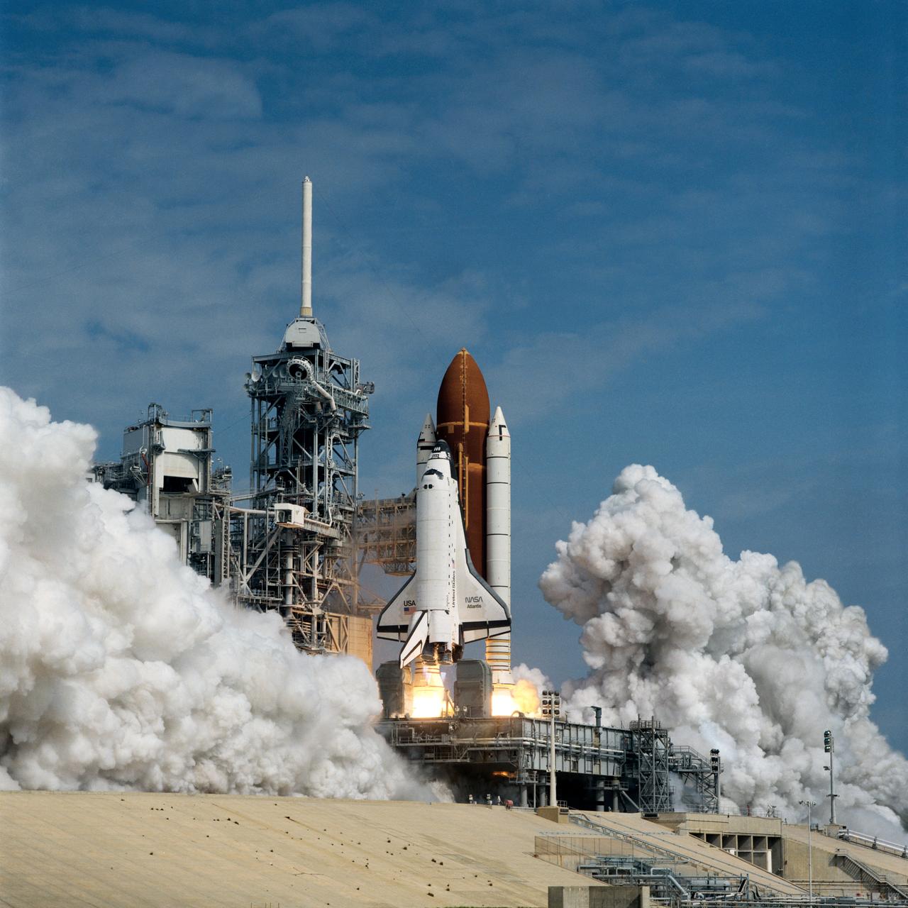 STS-37 Atlantis, Orbiter Vehicle (OV) 104, lifts off from Kennedy Space Center (KSC) Launch Complex (LC) Pad at 9:22:45:0439 (Eastern Standard Time (EST)). OV-104, atop its external tank (ET) and flanked by its two solid rocket boosters (SRBs), is captured just after space shuttle main engine (SSME) firing and as it rises above the mobile launcher platform. The fixed service structure (FSS) and retracted rotating service structure (RSS) appear along side OV-104. Clouds of exhaust smoke begin to fill the launch pad area.
