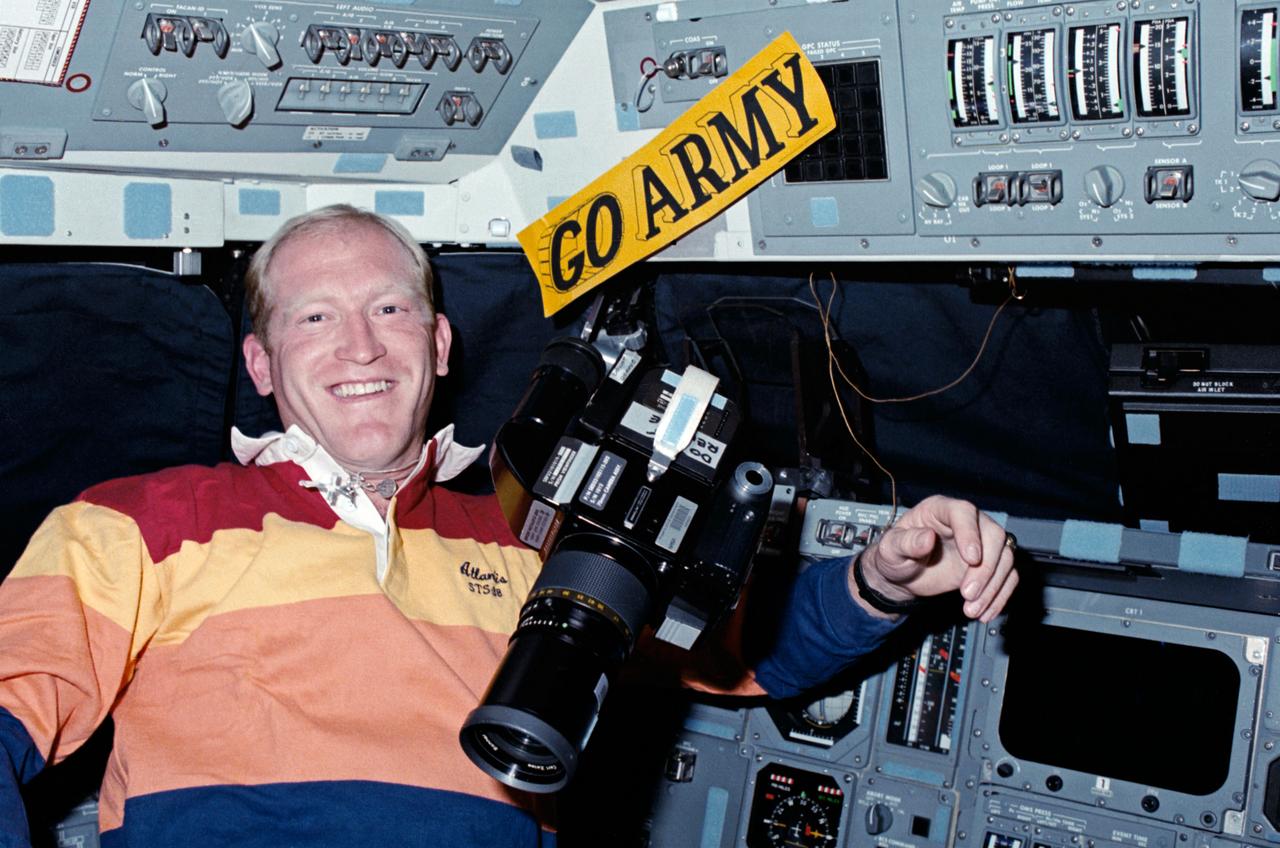 STS-38 Mission Specialist (MS) Charles D. Gemar freefloats in front of commanders station on the forward flight deck of Atlantis, Orbiter Vehicle (OV) 104, along with HASSELBLAD camera and "GO ARMY" decal.