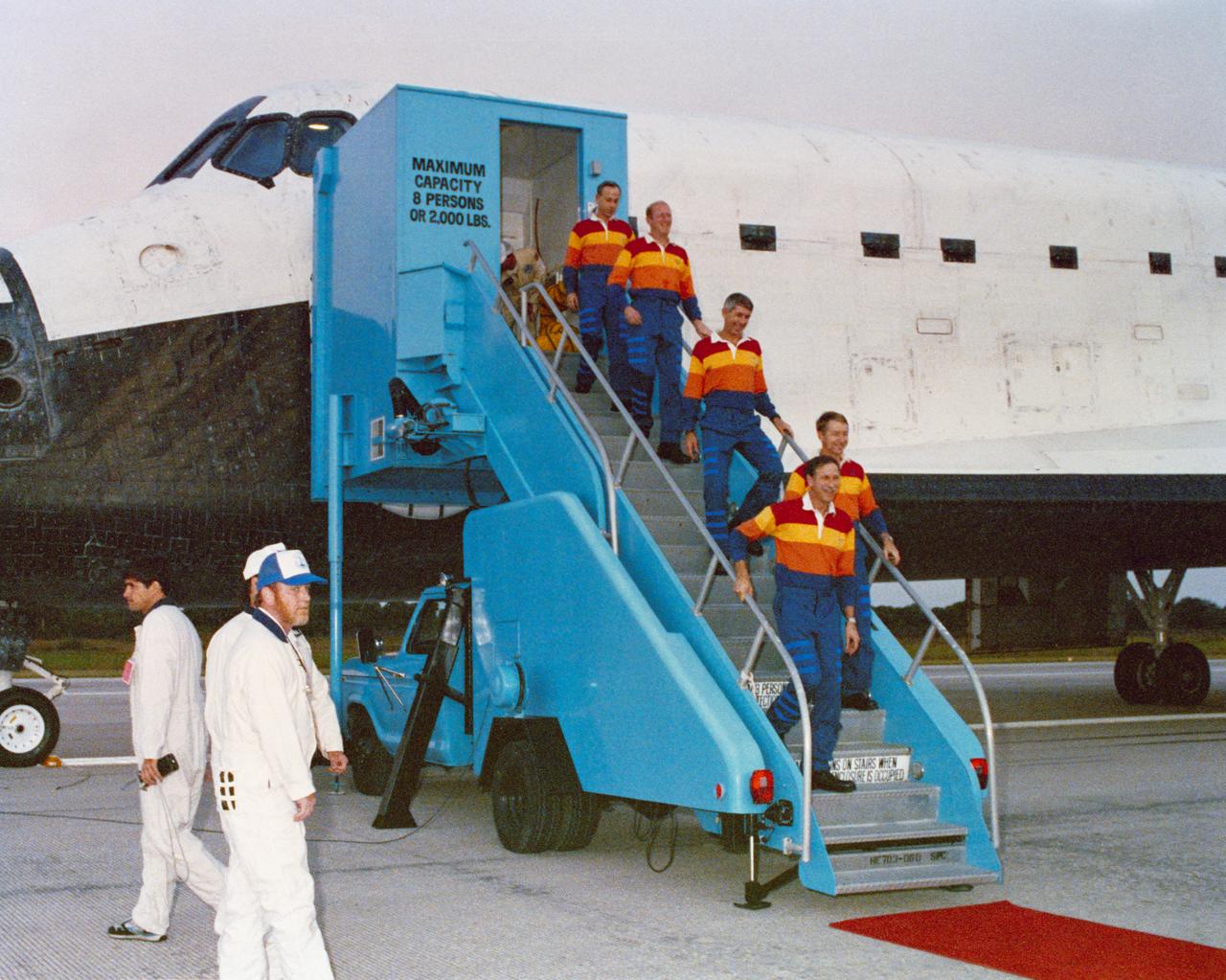 STS-38 crewmembers, wearing red, yellow, and orange polo shirts, egress Atlantis, Orbiter Vehicle (OV) 104, via a mobile stairway at the Kennedy Space Center's (KSC's) Shuttle Landing Facility (SLF). Commander Richard O. Covey, nearing the bottom of the stairway, is followed by Pilot Frank L. Culbertson, Mission Specialist (MS) Robert C. Springer, MS Charles D. Gemar, and MS Carl J. Meade. Ground servicing personnel look on in the foreground.