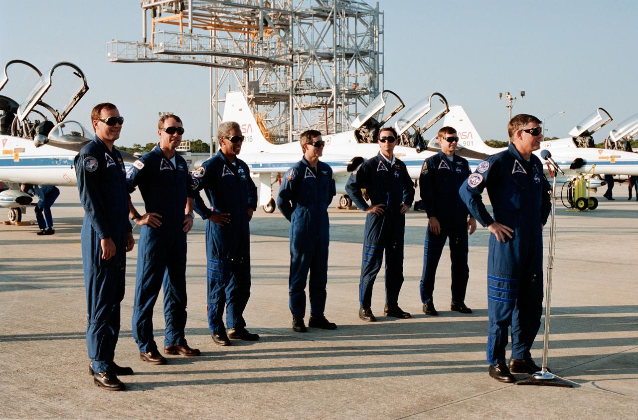 STS039-S-003 (20 April 1991) --- Astronaut Michael L. Coats (right) addresses the news media after arriving at the Shuttle Landing Facility along with his six fellow crewmembers.  From left are astronauts Richard J. Hieb, L. Blaine Hammond, Guion S. Bluford, Charles L.  (Lacy) Veach, Gregory J. Harbaugh and Donald R. McMonagle.  The Space Shuttle mate/demate stand is seen in the background.                Note: The STS-39 launch of Discovery occurred at 7:33:14 a.m. (EDT), April 28, 1991.