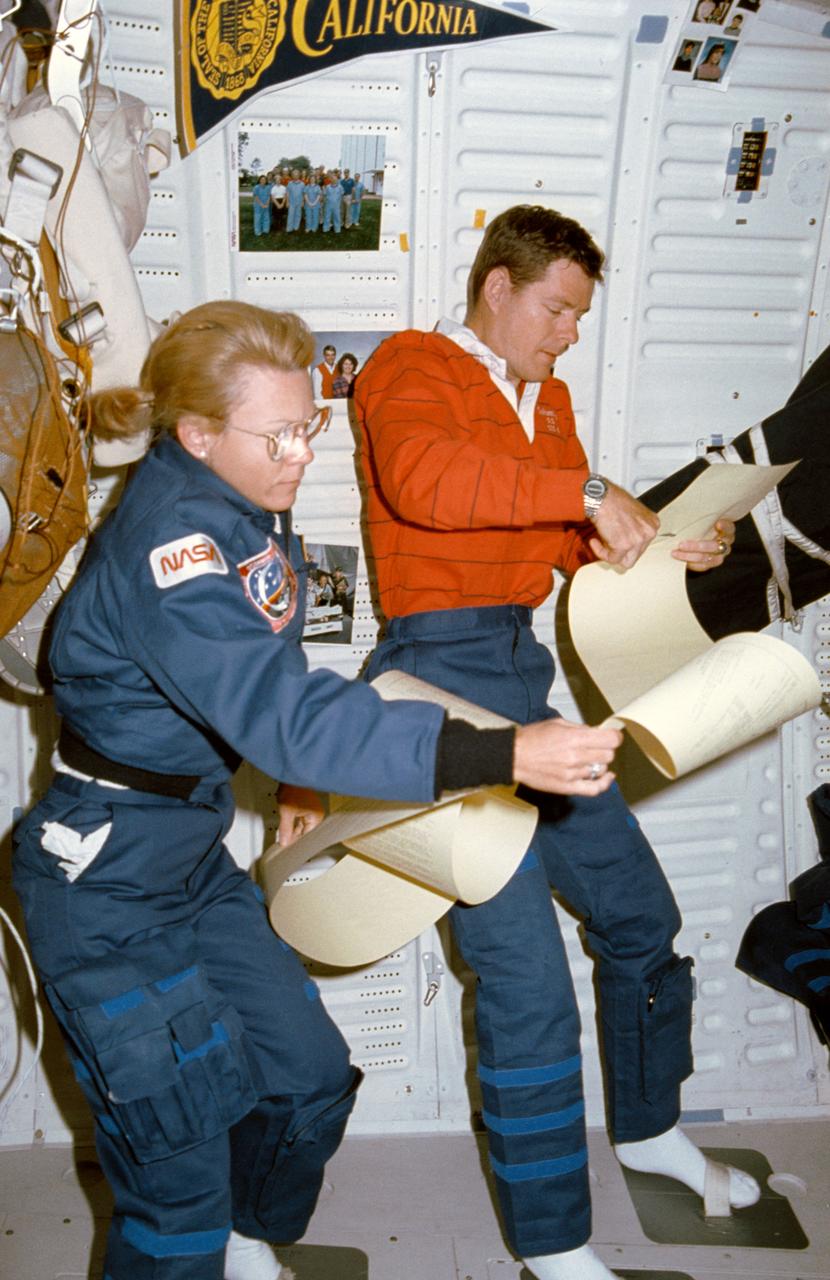 STS040-17-003 (5-14 June 1991) --- Astronauts Rhea Seddon and Bryan D. O'Connor share a 15 ft. length of teleprinter messages aboard Columbia.  During the nine-day Spacelab Life Sciences (SLS-1) mission, the STS-40 crewmembers received a large volume of similar print-outs from ground controllers.  Using foot restraints, the two obviously expect their perusing to take awhile.  This middeck scene was photographed with a 35mm camera.