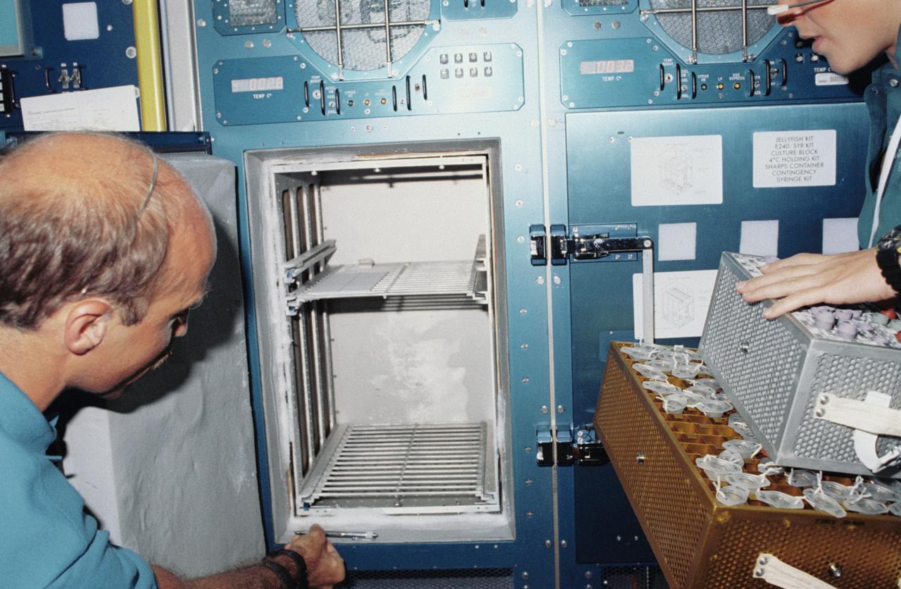 STS040-202-033 (5-14 June 1991) --- A medium closeup scene shows astronaut James P. Bagian (left) and an unidentified crewmember (partially out of frame) looking at a vacant refrigerator in the Spacelab Life Sciences (SLS-1) module aboard the Earth-orbiting Space Shuttle Columbia.  Following the detection of problems with the refrigerator, its contents were temporarily removed.  This scene was photographed with a 35mm camera.