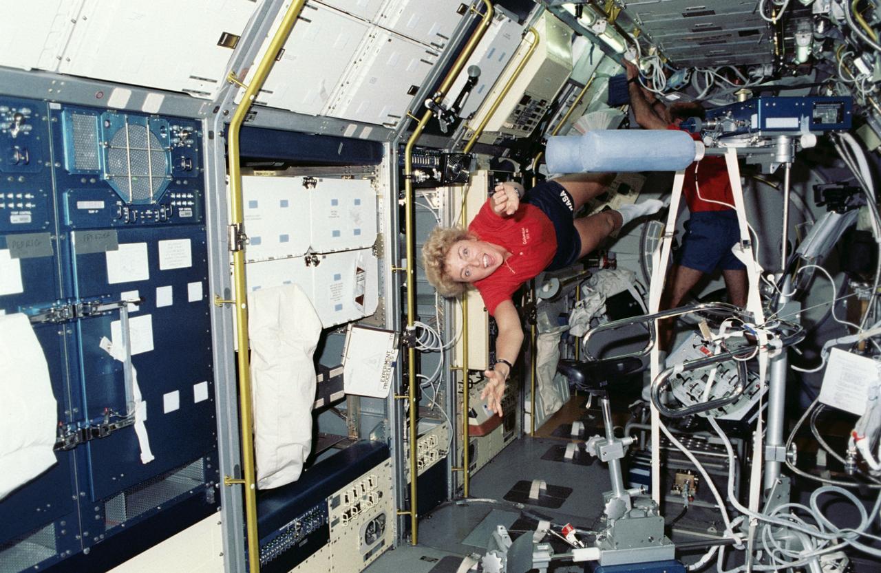 STS040-212-006 (5-14 June 1991) --- Payload specialist Millie Hughes-Fulford floats through the Spacelab Life Sciences (SLS-1) module aboard the Earth-orbiting Columbia.  Astronaut James P. Bagian, mission specialist, is at the blood draw station in the background.  The scene was photographed with a 35mm camera.