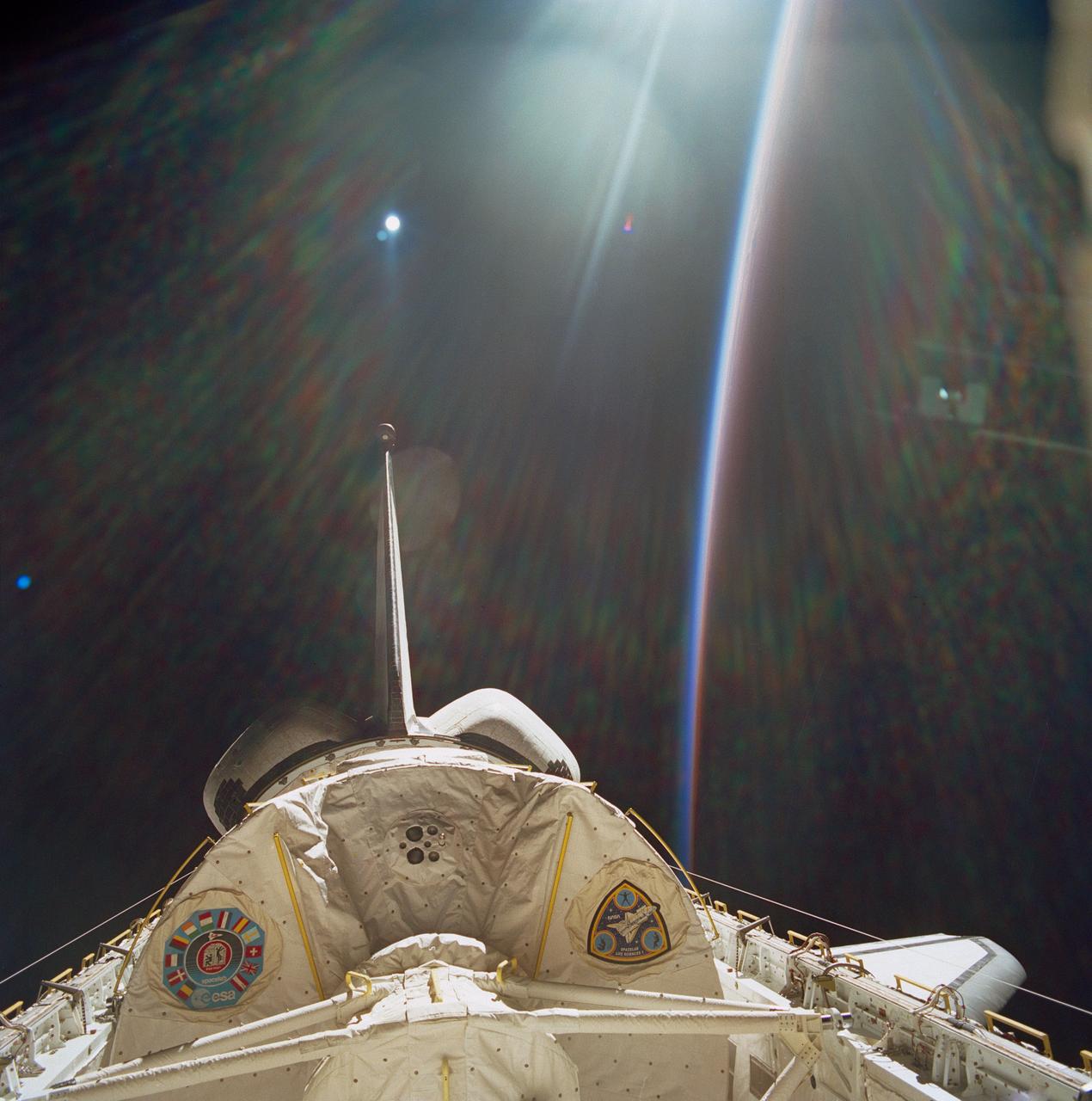 STS040-612-005 (5-14 June 1991) --- This view showing the Spacelab Life Sciences (SLS-1) module in Columbia's cargo bay was taken through windows on the aft flight deck.  Under some lighting conditions the multi-layered Shuttle windows have internal reflections that provide a kaleidoscopic effect.  In this image the sunrays as seen on the clouds also appear to be present in space.  Note how the white sunlight toward the Sun at the Earth's limb becomes separated into the colors of the visible spectrum towards that part of the limb further into darkness due to atmosphere acting as a natural prism.