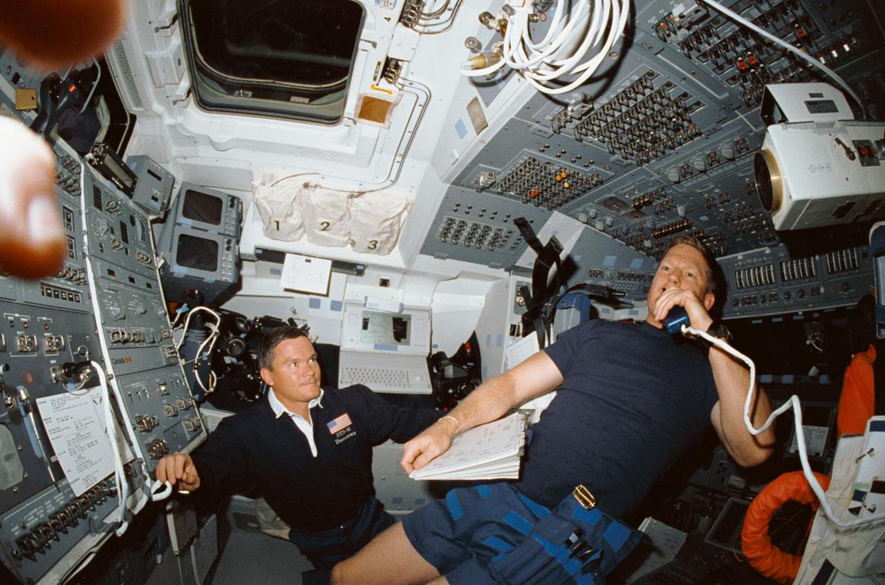 STS041-02-035 (6-10 Oct 1990) --- A fish-eye lens view shows two of STS-41's three mission specialists on the flight deck of Discovery.  Astronaut William M. Shepherd, right, communicates with ground controllers as Astronaut Bruce E. Melnick looks on.