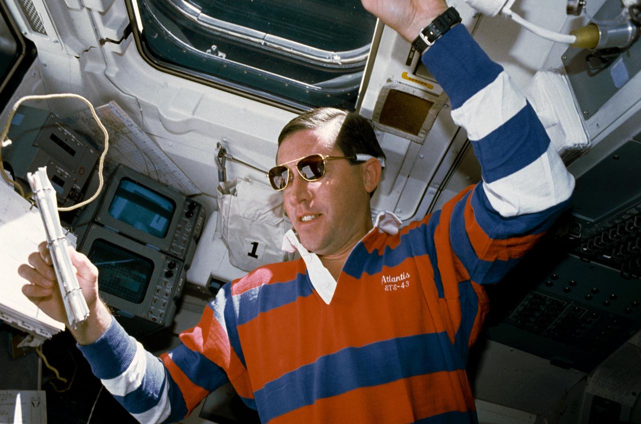 STS043-04-032 (11 Aug 1991) --- STS-43 Pilot Michael A. Baker, wearing sunglasses, reviews a checklist on the aft flight deck of Atlantis, Orbiter Vehicle (OV) 104. He is monitoring data associated with the Space Station Heat Pipe Advanced Radiator Element II (SHARE-II) located in OV-104's payload bay (PLB) from his position in front of the aft flight deck viewing windows. Behind Baker are the closed circuit television (CCTV) monitors and above his head is overhead window W8.