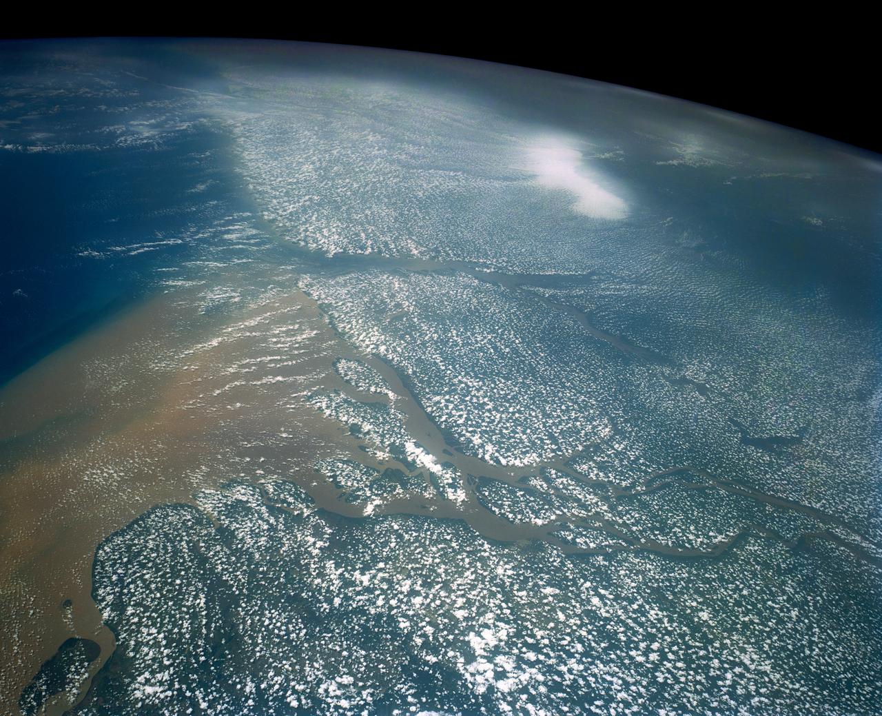 Huge sediment loads from the interior of the country flow through the Mouths of the Amazon River, Brazil (0.5S, 50.0W). The river current carries hundreds of tons of sediment through the multiple outlets of the great river over 100 miles from shore before it is carried northward by oceanic currents. The characteristic "fair weather cumulus" pattern of low clouds over the land but not over water may be observed in this scene.