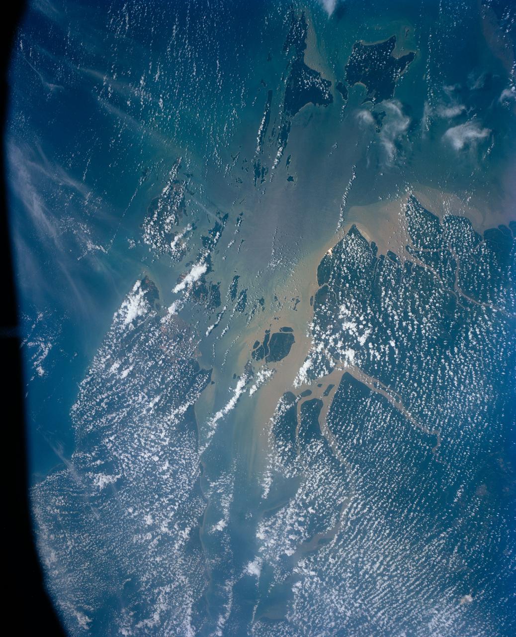 This view shows the area around Northeastern Sumatra, Indonesia (1.0N, 104.0E). The city of Singapore and the Singapore Strait is in the center at the southern tip of the Malay Peninsula. The Singapore Strait is the eastern extension of the Strait of Malacca and separates the Malay Peninsula from Sumatra. Large sediment plumes from the rivers attest to the local soil erosion and industrial dumping ofd wastes.