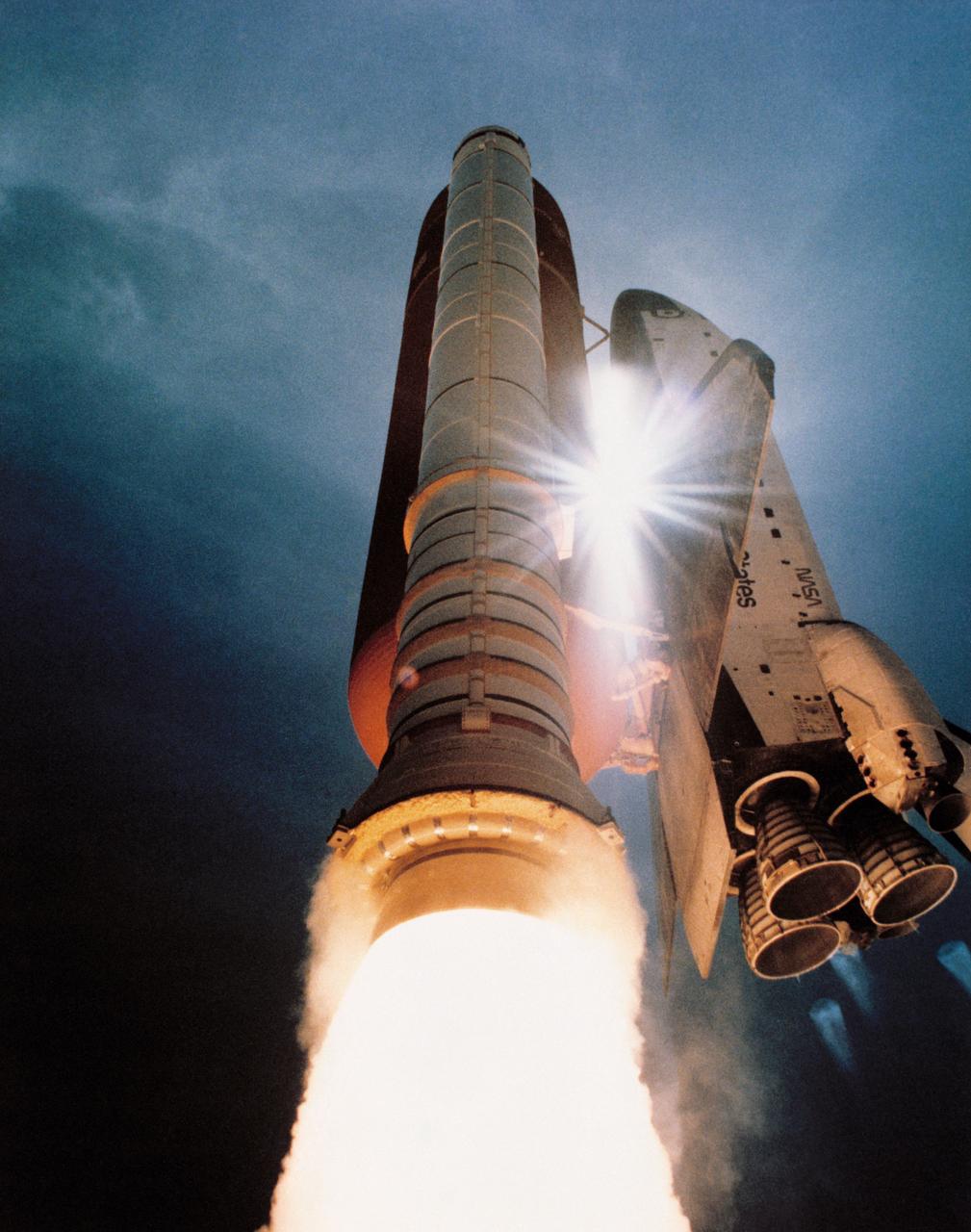 STS-43 Atlantis, Orbiter Vehicle (OV) 104, soars toward space after liftoff from Kennedy Space Center (KSC) Launch Complex (LC) Pad 39A at 11:02: 00 am (Eastern Daylight Time (EDT)). This low angle view captures OV-104 as it begins its roll maneuver. A burst of sunlight shines through the mated hardware elements supporting the Space Shuttle Atlantis for the STS-43 mission's launch phase. Exhaust plumes billow from the solid rocket booster (SRB) skirts. All three space shuttle main engines (SSMEs) glow as they power OV-104 into orbit. The bottom of external tank (ET) is highlighted by the SRB/SSME firings. This image was selected by the Public Affairs Office (PAO) for public release.