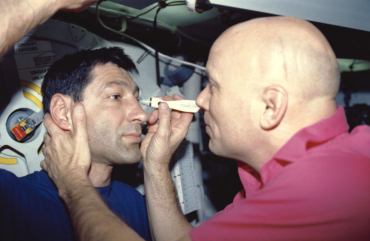 STS044-04-001 (24 Nov-1 Dec 1991) --- Astronauts F. Story Musgrave (right) and Mario Runco, Jr., mission specialists, team up for one of the biomedical Detailed Supplementary Objective (DSO) test on the eight-day flight, this one involving intraocular pressure.