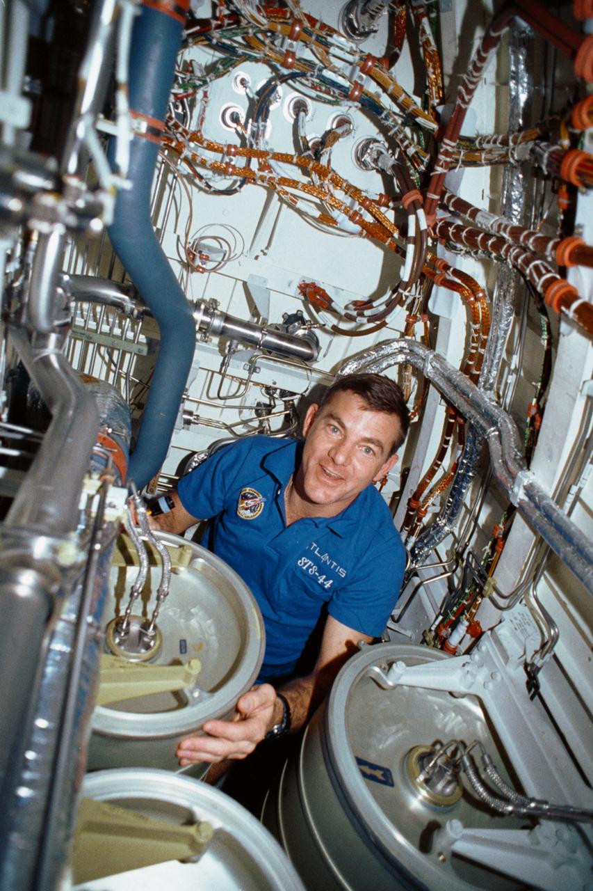 STS-44 Mission Specialist (MS) James S. Voss works under the middeck subfloor of Atlantis, Orbiter Vehicle (OV) 104, to repair humidity separator leakage problems. Voss is surrounded by several water tanks and a maze of shuttle wiring and plumbing. Voss earned the nickname of "Bilge Man" because of his time spent on the lower deck tending to the leakage problem. This is the first photo released of a crewmember in this area of the shuttle.