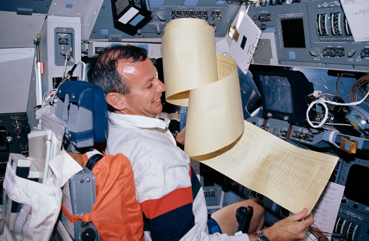 STS045-02-020 (24 March-2 April 1992) --- Brian Duffy, STS-45 pilot, struggles with a large volume of data printouts from the teleprinter system.  He is seated at the commander's station on the flight deck of the Earth-orbiting Atlantis during the nine-day mission.  This frame was taken with a 35mm camera.