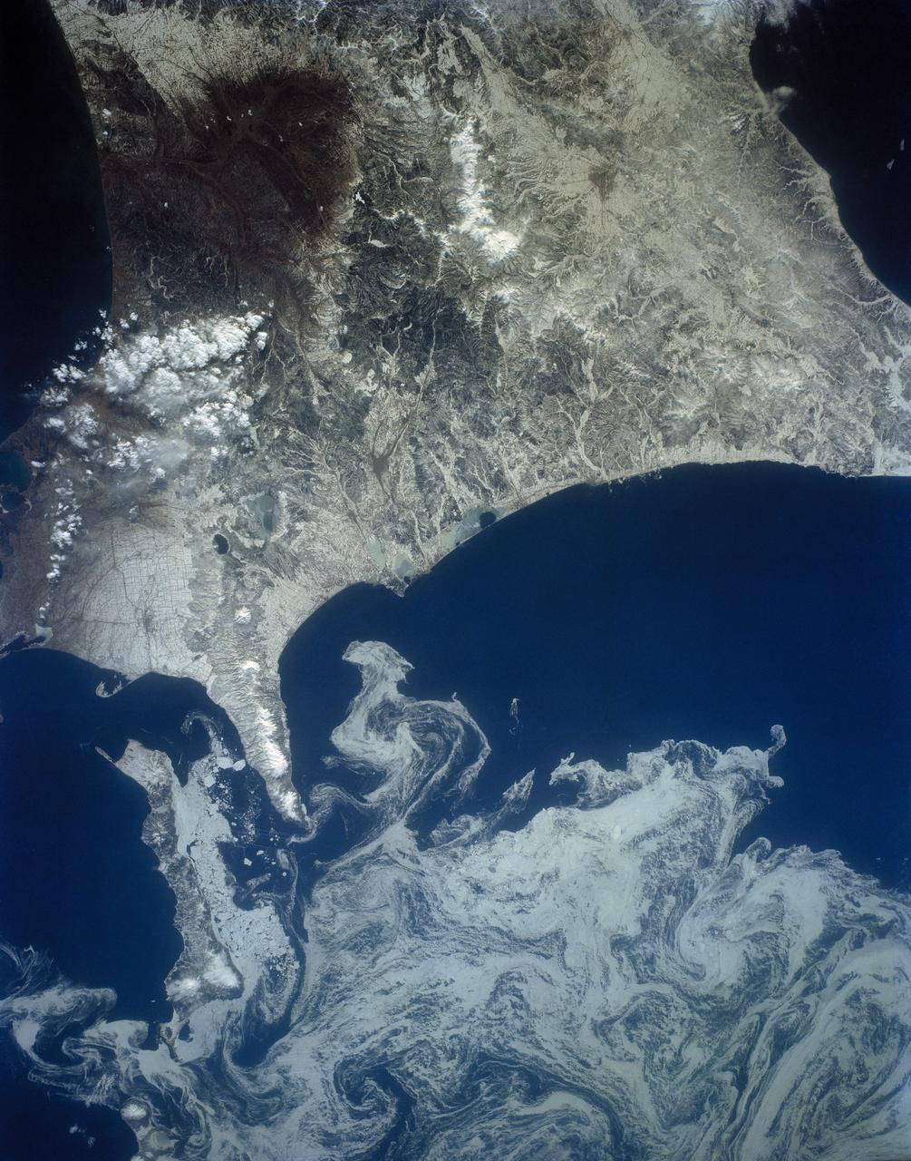 The northeast coast of Hokkaido and Kunashir Island, Japan (44.0N, 143.0E) are seen bordered by drifting sea ice. The sea ice has formed a complex pattern of eddies in response to surface water currents and winds. Photos of this kind aid researchers in describing local ocean current patterns and the effects of wind speed and direction on the drift of surface material, such as ice floes or oil. Kunashir is the southernmost of the Kuril Islands.