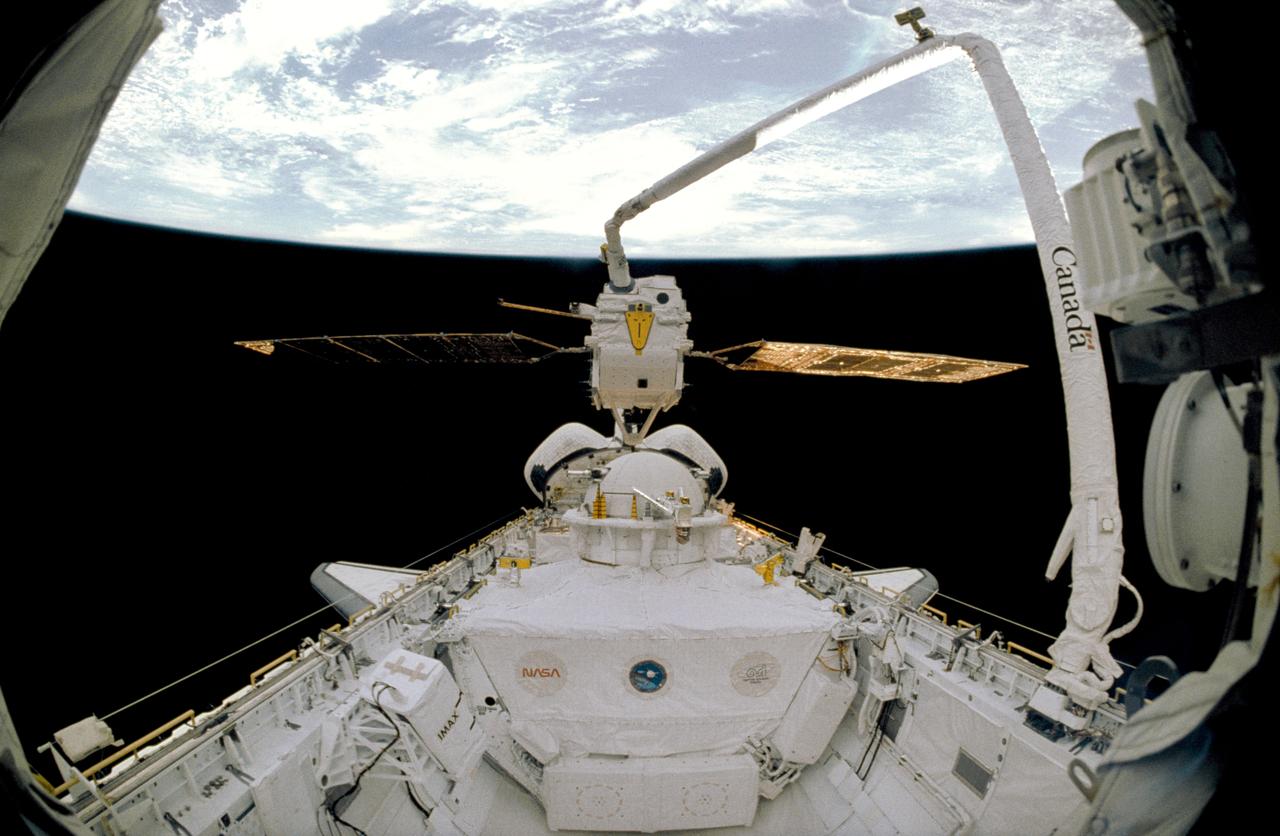 STS046-08-010 (1 Aug 1992) --- The EURECA satellite is hoisted above the Space Shuttle Atlantis' cargo bay by the Remote Manipulator System (RMS) during early mission activity aboard the Earth-orbiting Shuttle. A 16mm lens gives this 35mm frame a "fish-eye" effect. The Tethered Satellite System (TSS), center frame, is stowed in the cargo bay, where it awaits extensive operations by the seven-member crew.