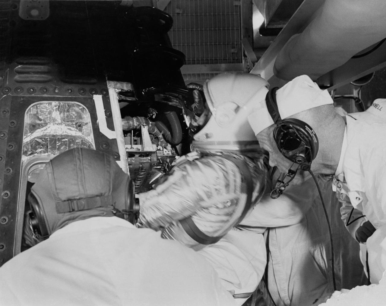 S61-02881 (1961) --- Astronaut Virgil I. (Gus) Grissom, suited up in a newly designed pressure suit, is assisted as he climbs into Liberty Bell 7 spacecraft. Behind him backup pilot John Glenn watches the insertion. The Mercury-Redstone 4 (MR-4) mission was scrubbed a few hours later due to unfavorable weather over the launch pad. Photo credit: NASA