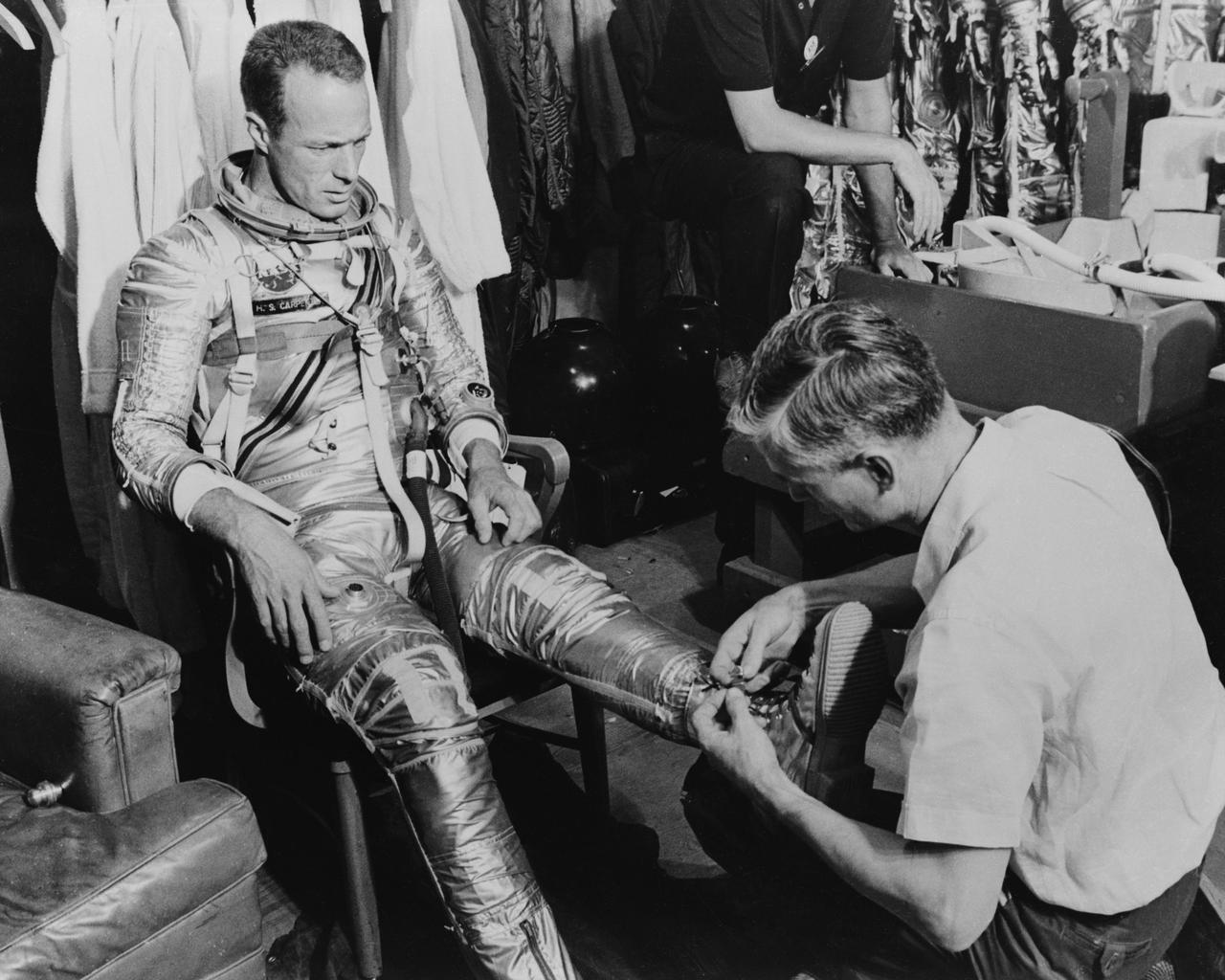 S61-03513 (1961) --- Mercury astronaut M. Scott Carpenter, prime pilot for the Mercury-Atlas 7 (MA-7) spaceflight, and Crew Equipment Specialist Joe Schmitt are pictured during a suiting exercise. Schmitt is seen lacing up Carpenter's boots. Photo credit: NASA