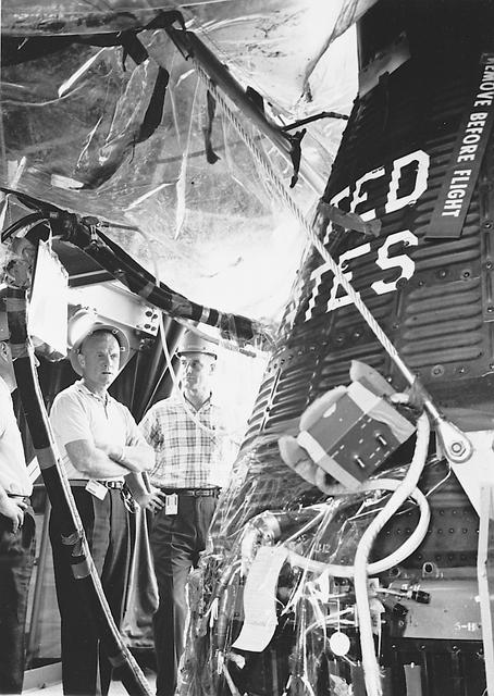 Astronauts John H. Glenn Jr. (center), and John Peterson (right), in gantry viewing Mercury Spacecraft during assembly. CAPE CANAVERAL, FL B&W