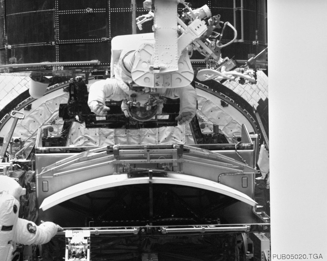 S61-E-016 (6 Dec 1993) --- Astronaut Jeffrey A. Hoffman (frame center) remains secured by his feet on the end of Endeavour's robot arm as he prepares to participate in the replacement of Hubble Space Telescope's Wide Field/Planetary Camera (WF/PC). Astronaut F. Story Musgrave (just in frame at lower left corner) assists Hoffman in removing the new camera (WFPC-II) from the Scientific Instrument Protective Enclosure (SIPE). Electronic still photography is a relatively new technology which provides the means for a handheld camera to electronically capture and digitize an image with resolution approaching film quality. The electronic still camera has flown as an experiment on several other shuttle missions.