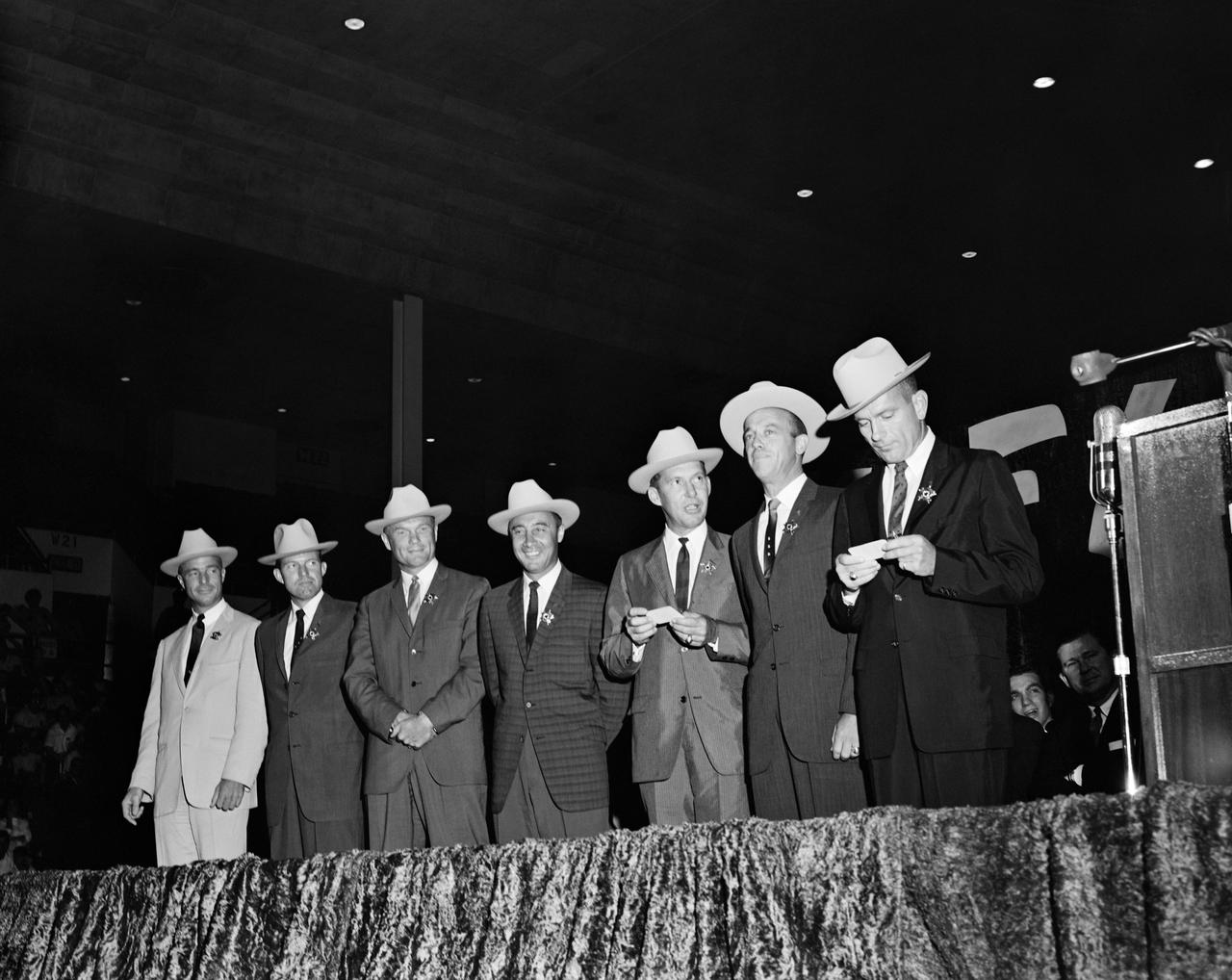 S62-03709 (4 July 1962) --- The original seven Mercury astronauts, each wearing new cowboy hats and a badge in the shape of a star, are pictured on stage at the Sam Houston Coliseum. A large crowd was on hand to welcome them to Houston, Texas. Left to right are astronauts M. Scott Carpenter, L. Gordon Cooper Jr., John H. Glenn Jr., Virgil I. Grissom, Walter M. Schirra Jr., Alan B. Shepard Jr., and Donald K. Slayton. Sen. John Tower (R.-Texas) is seen in far right background. Photo credit: NASA