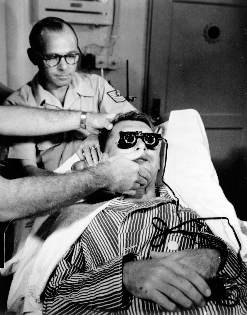 S62-06157 (1962) --- Astronaut Walter Schirra Jr. gets modified calonic test. His balance mechanism (semicircular canals) are tested by running cool water into ear and measuring effect on eye motions (nystagmus) after his six-orbit flight in the Sigma 7 spacecraft. Photo credit: NASA