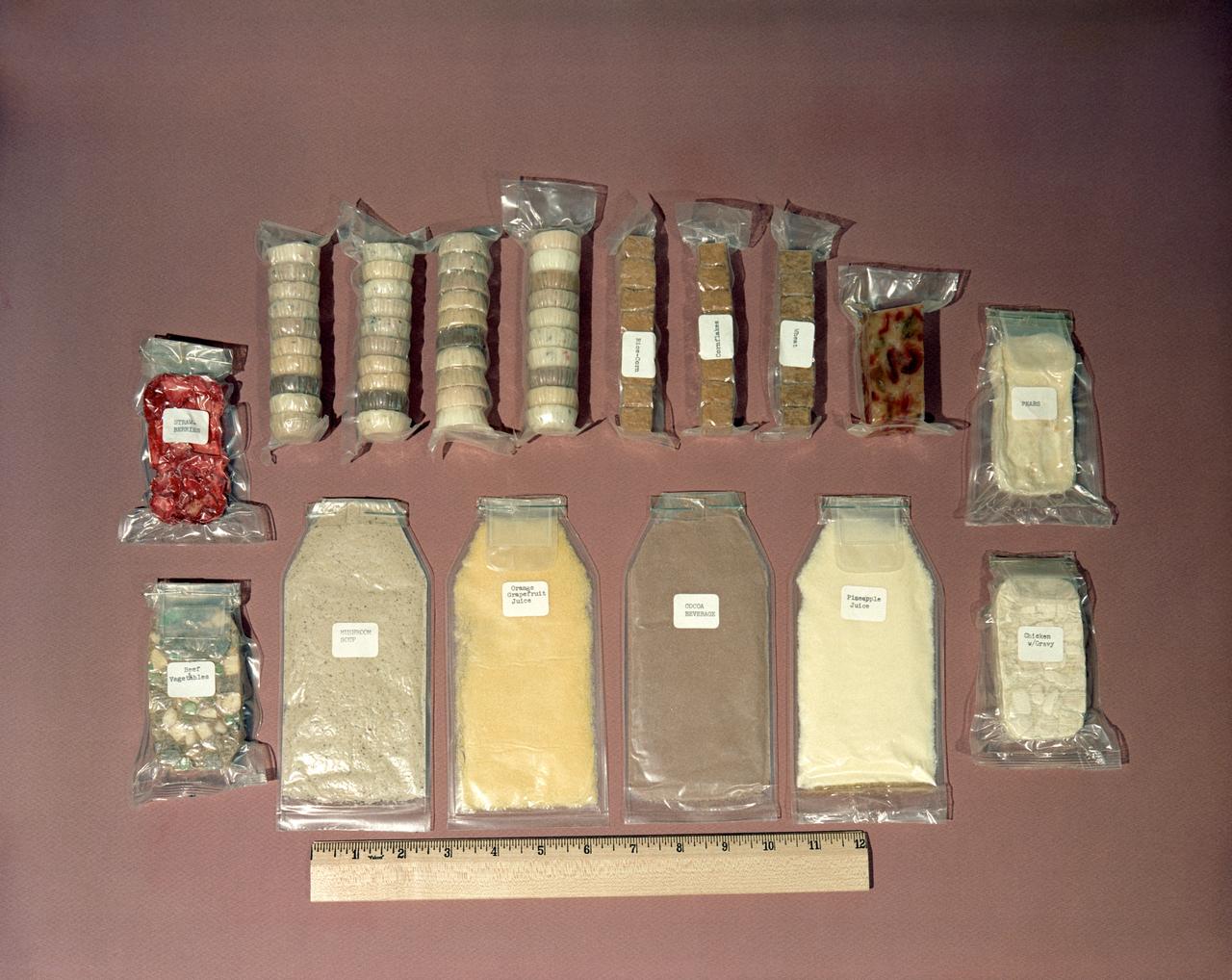 S62-08742 (1962) --- Food kit used by Mercury astronauts. Some is dehydrated and needs water, other packets are ready to eat. Size is measured relative to a ruler. Included are packets of mushroom soup, orange-grapefruit juice, cocoa beverage, pineapple juice, chicken with gravy, pears, strawberries, beef and vegetables and other assorted food containers. Photo credit: NASA