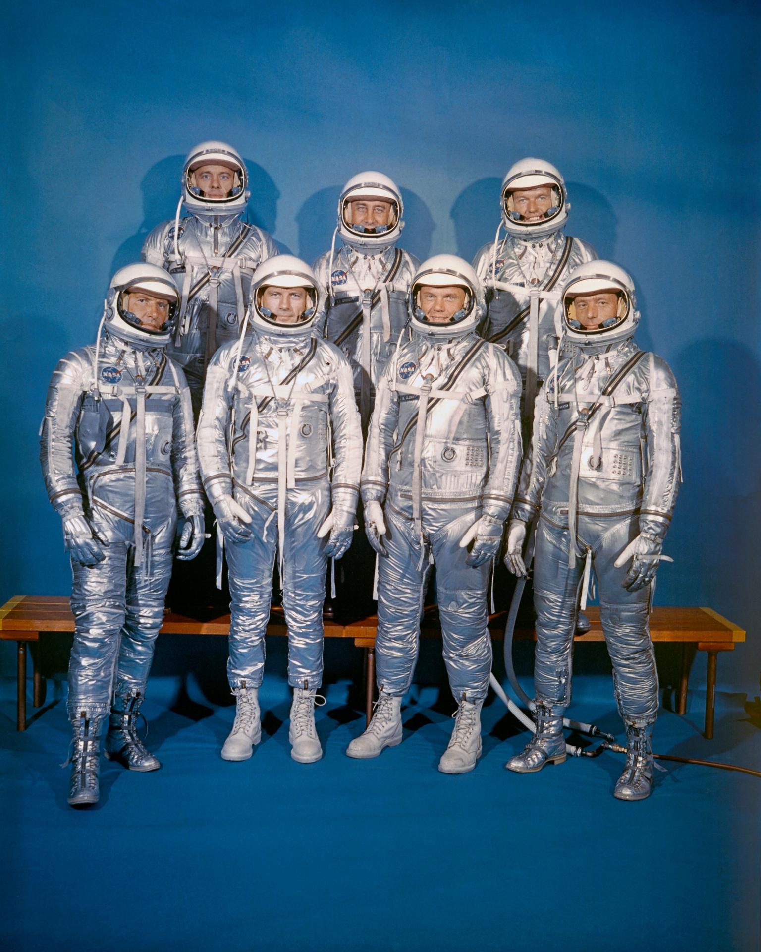 Seven men wearing silver astronaut spacesuits