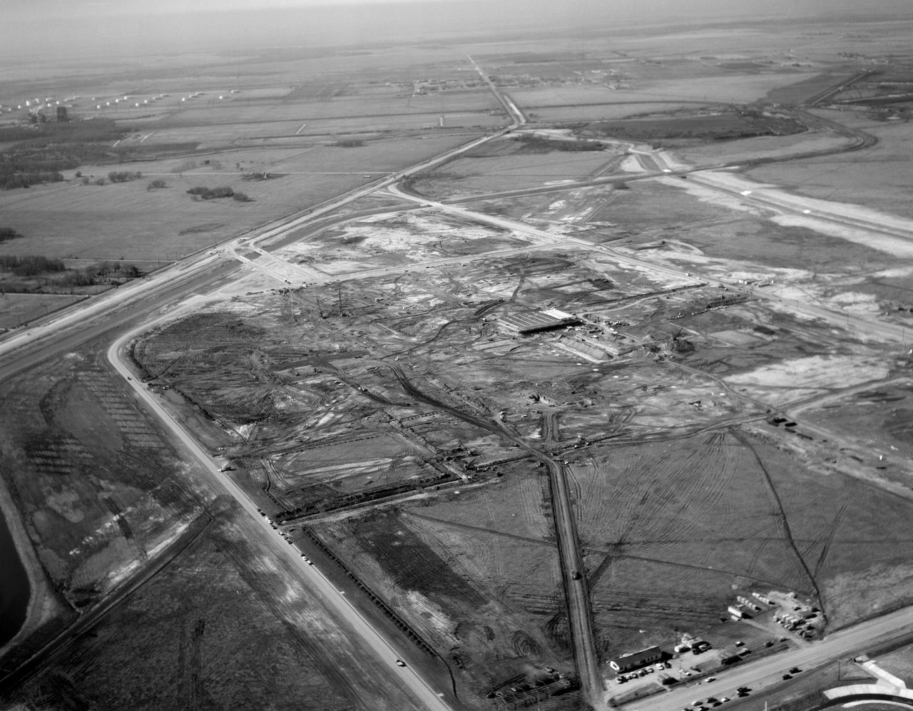 S63-01074 (1963) --- A black and white aerial view of Site 1, the Manned Spacecraft Center, in 1963 during early construction. The view faces the southwest. Highway 528 is at the top of the picture. Second Street runs basically north and south on the right side of the image, to the right or west and running parallel to that avenue is a drainage ditch. Winding through the site a Houston Lighting and Power Co. canal crosses over the drainage ditch near the top of the frame. Twin bridges over the canal are pictured at upper left which were constructed to allow traffic to enter and leave through MSC's secondary gateway.  In frame center, construction appears very far along on the Central Data Office.