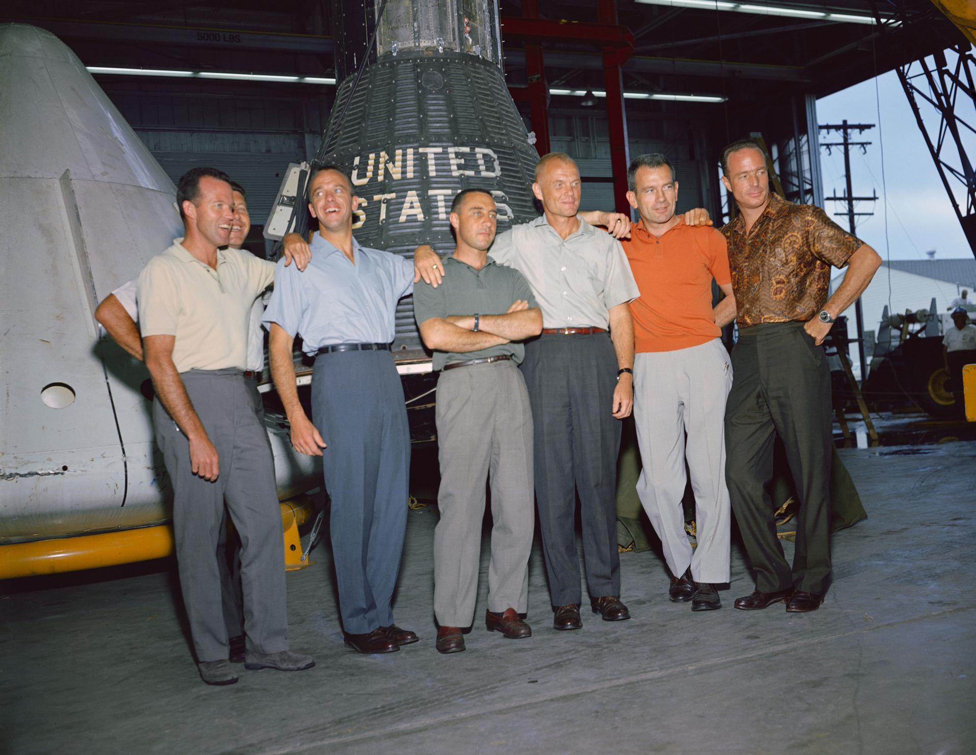 The Mercury 7 astronauts stand in front of a Mercury capsule for a photo at the Manned Spacecraft Center in Texas