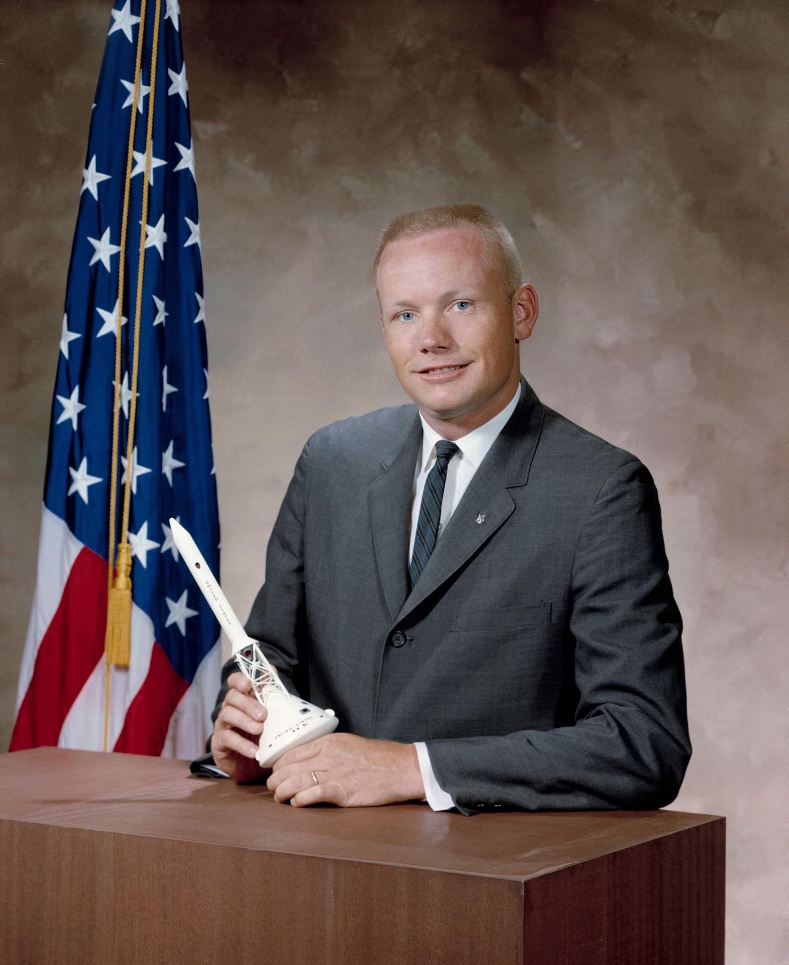 A man sitting at a table holding a model of a rocket with the American flag in the background