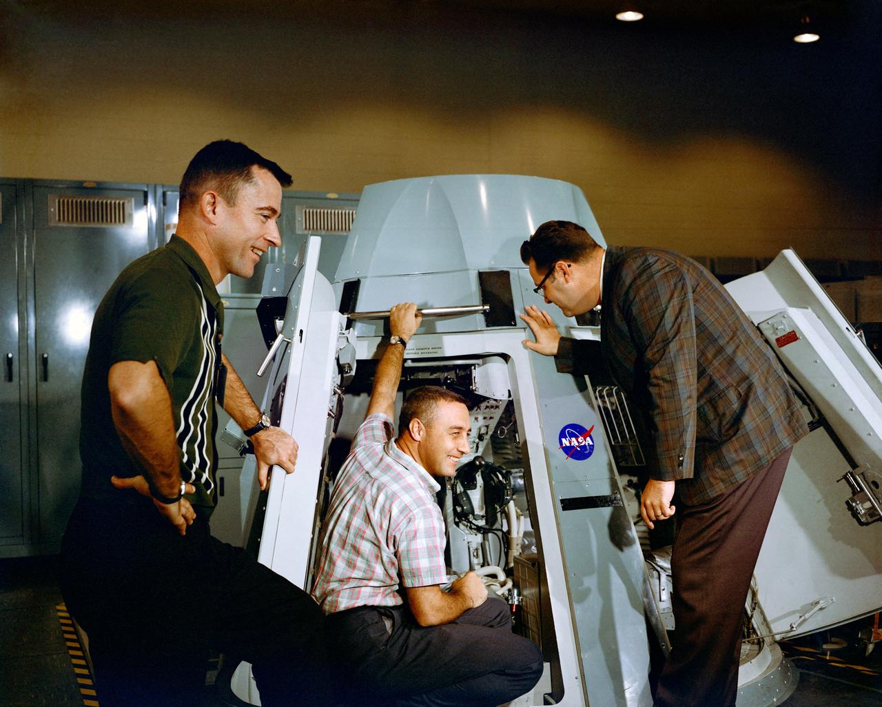 S64-40294 (19 Nov. 1964) --- Astronauts Virgil I. Grissom (center) and John W. Young (left), prime crew for the Gemini-Titan 3 mission, are shown inspecting the inside of Gemini spacecraft at the Mission Control Center at Cape Kennedy, Florida. Riley D. McCafferty is at right. Photo credit: NASA