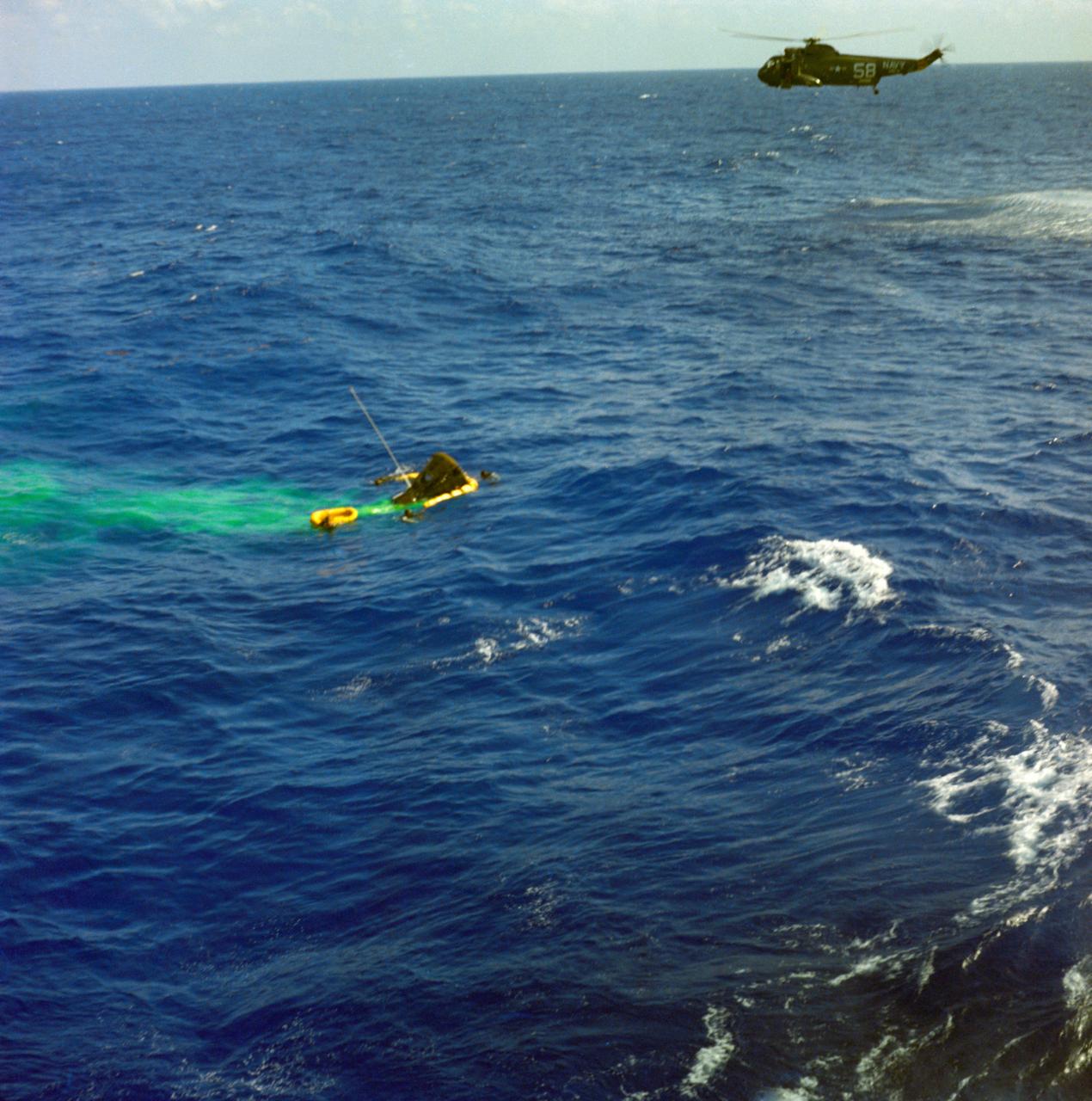 S65-18645 (23 March 1965) --- Navy swimmers are shown attaching a flotation collar to the Gemini-Titan 3 (GT-3) spacecraft during recovery operations following the successful flight. A helicopter hovers in the background. Astronauts Virgil I. Grissom and John W. Young are still in the spacecraft.
